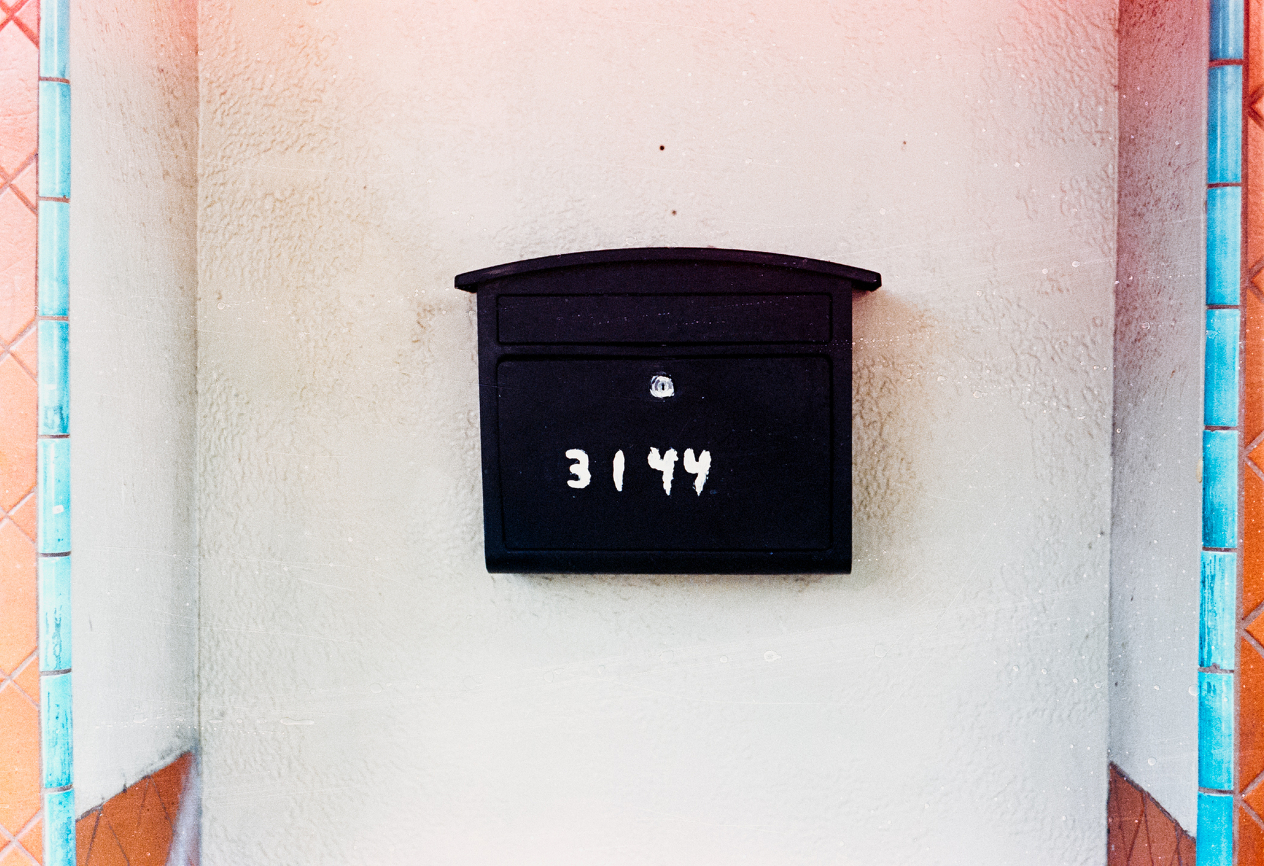 a scan of a color photograph of a door sign in the Mission in San Francisco. it says 3144 on a black mailbox, and is surrounded by a pink wall