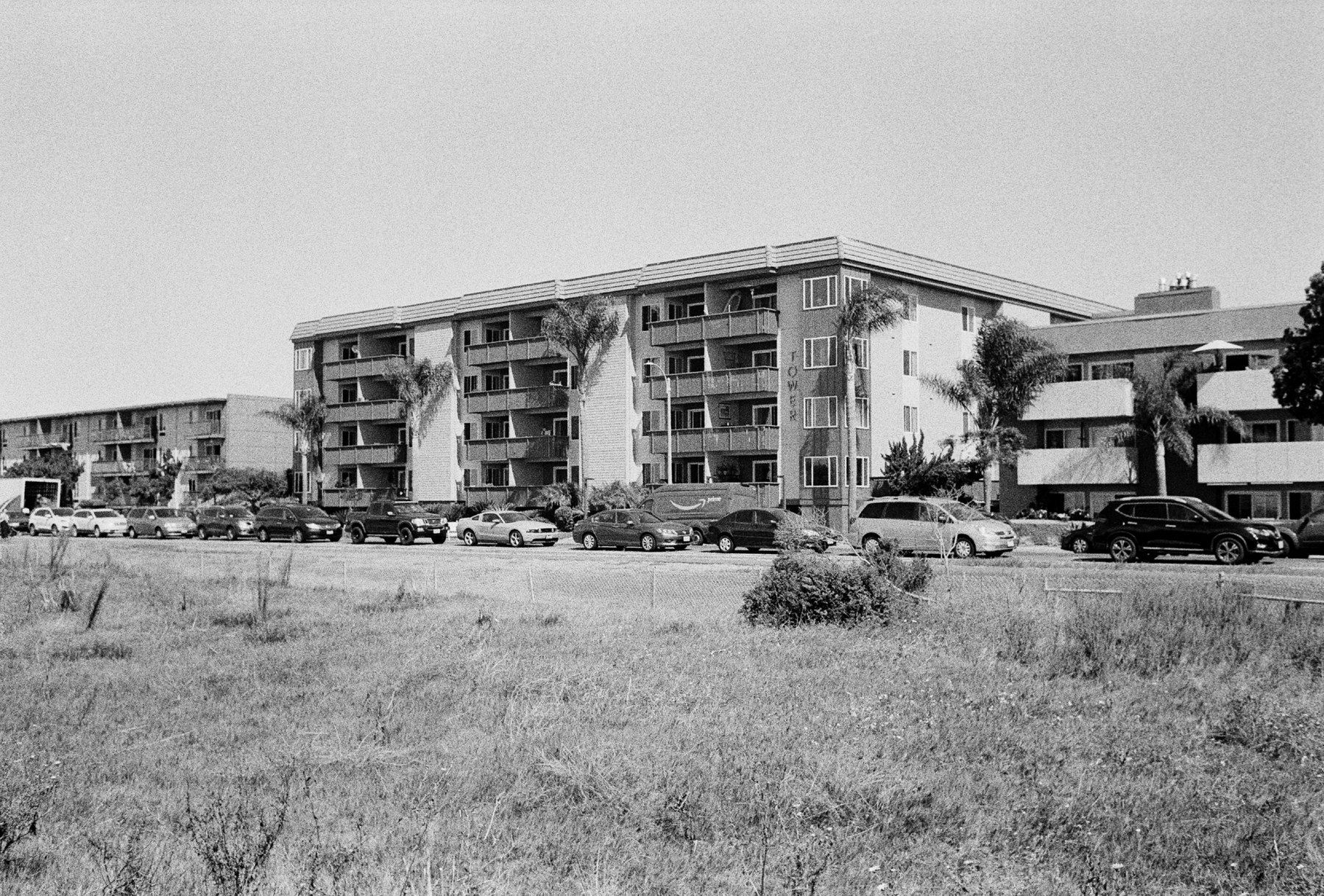 a scan of a black and white photo showing some blocky apartments lined with cars outside