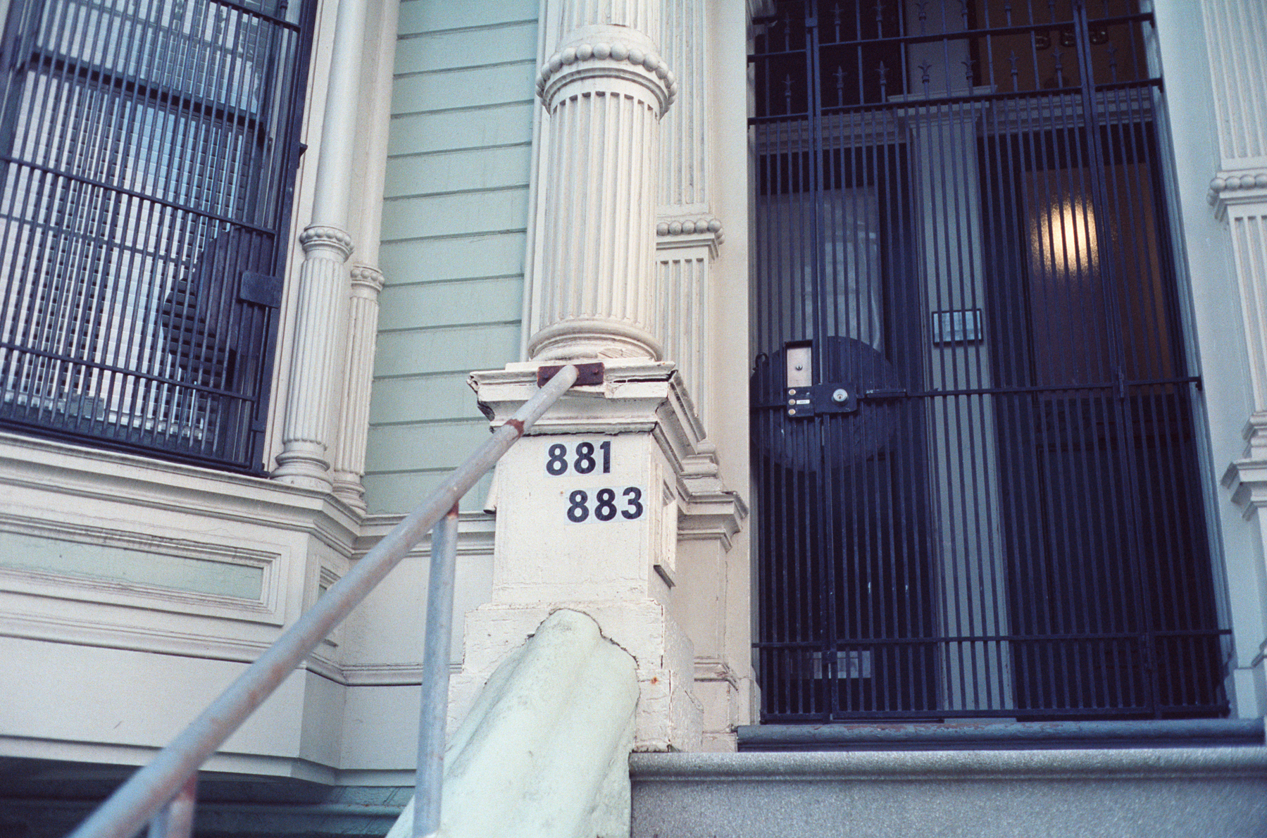 a scan of a color photograph of  the stairs and front doors of a Victorian house in San Francisco that is mostly blue. A few numbers say 881 and 883