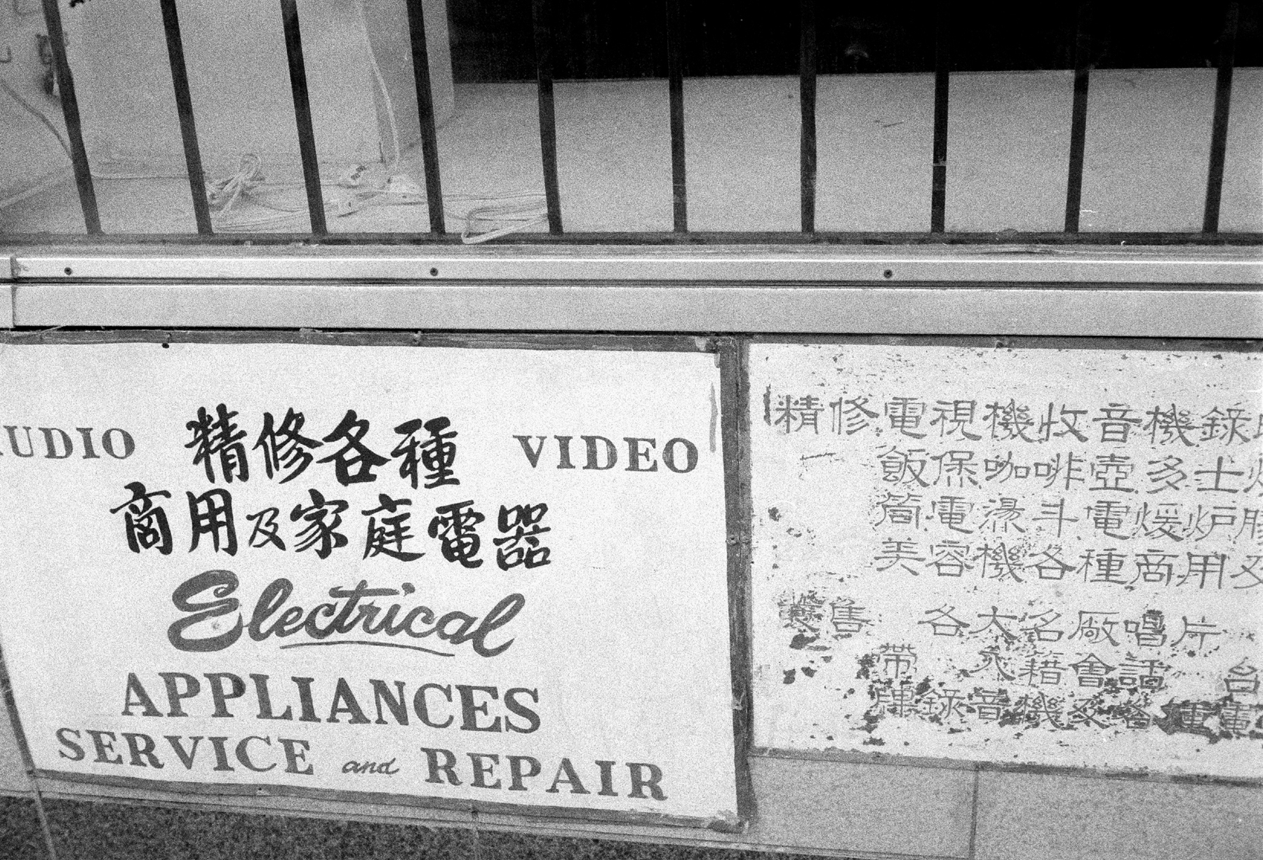 a scan of a black and white photo showing a vintage sign in English and Chinese characters mentioning audio video repair services