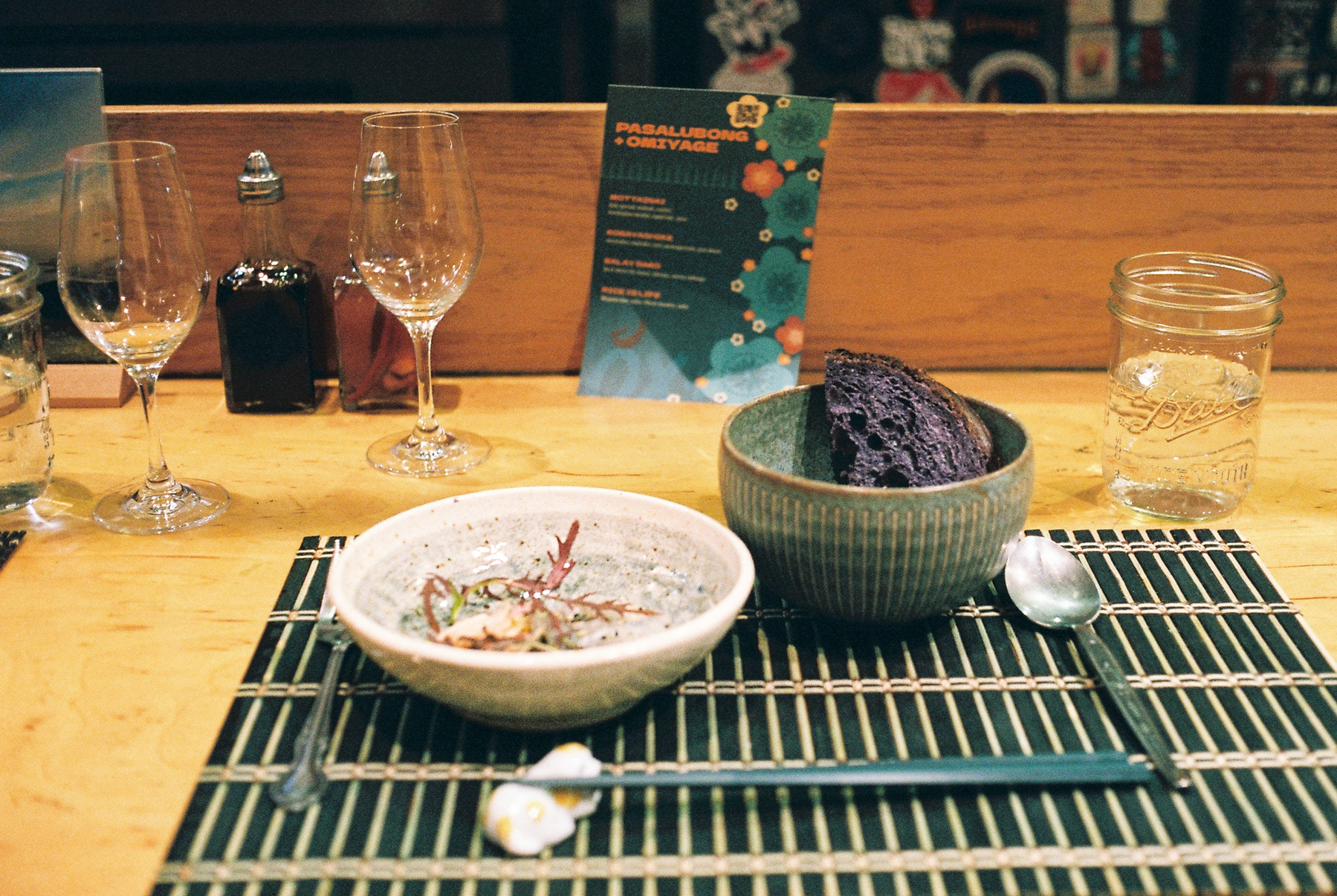a scan of a color photo of sashimi and ube bread on the table with Japanese mat and placements