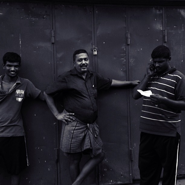 A black and white photo of three men wearing lungis posing against a wall