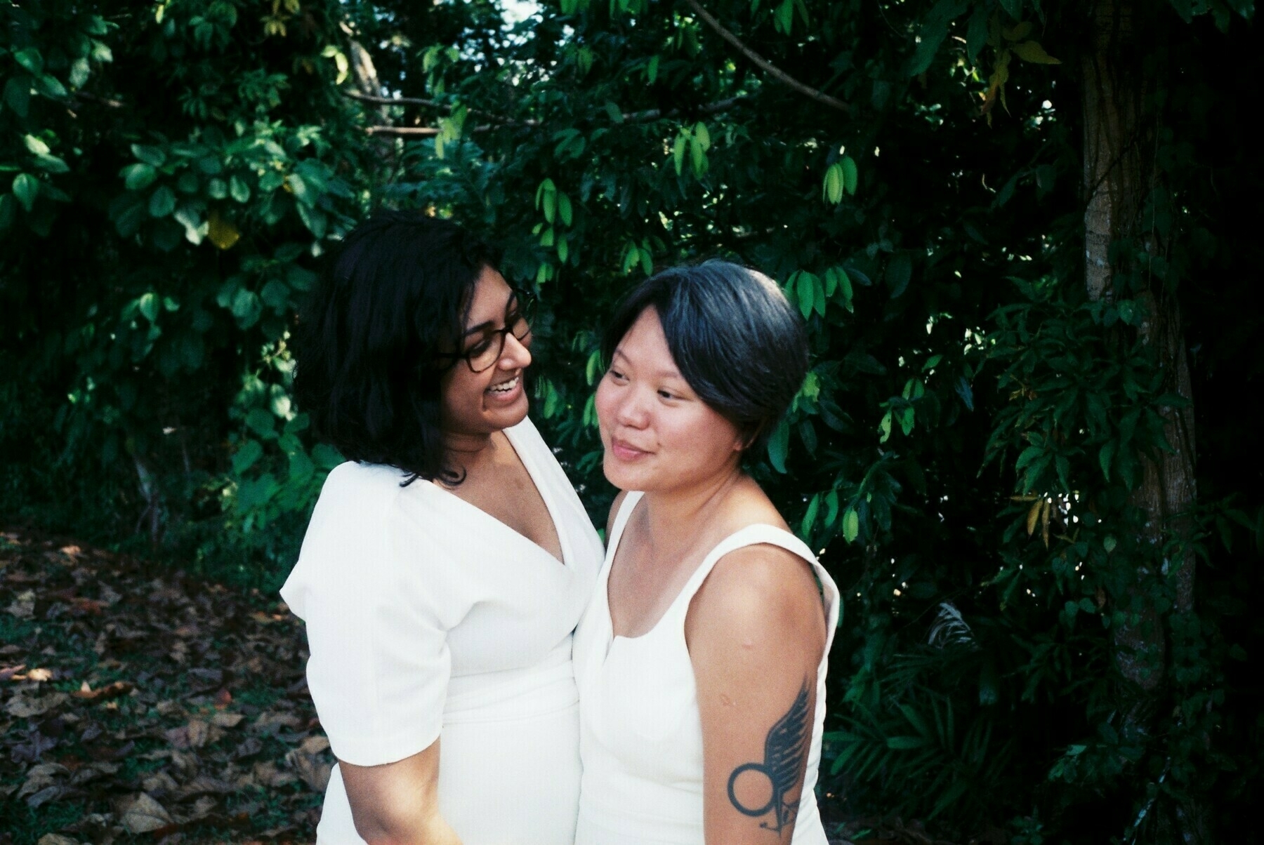 a color photo of a queer female couple in wedding whites in a jungle setting