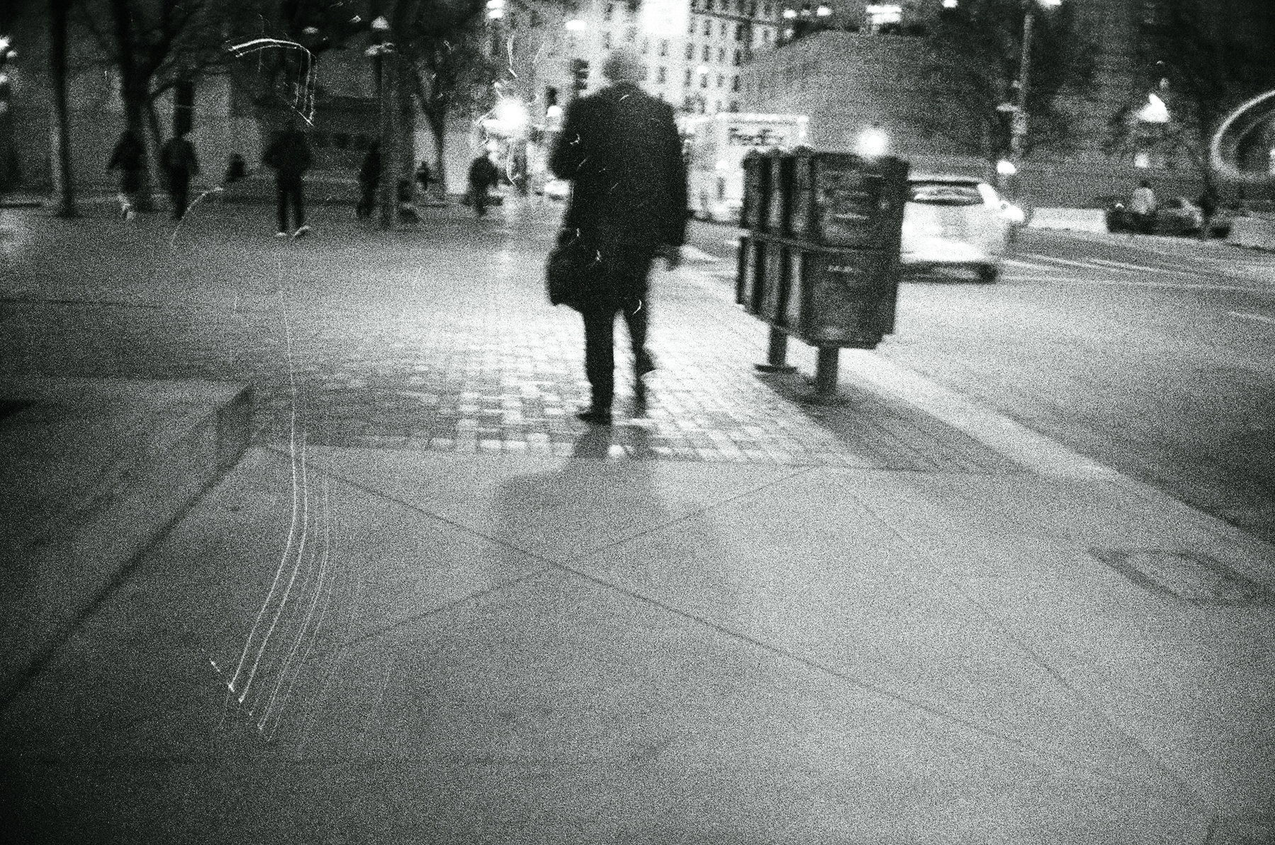 a scan of a black and white photograph of a person walking down a street in downtown San Francisco, there are streaks of light around the film negative scan