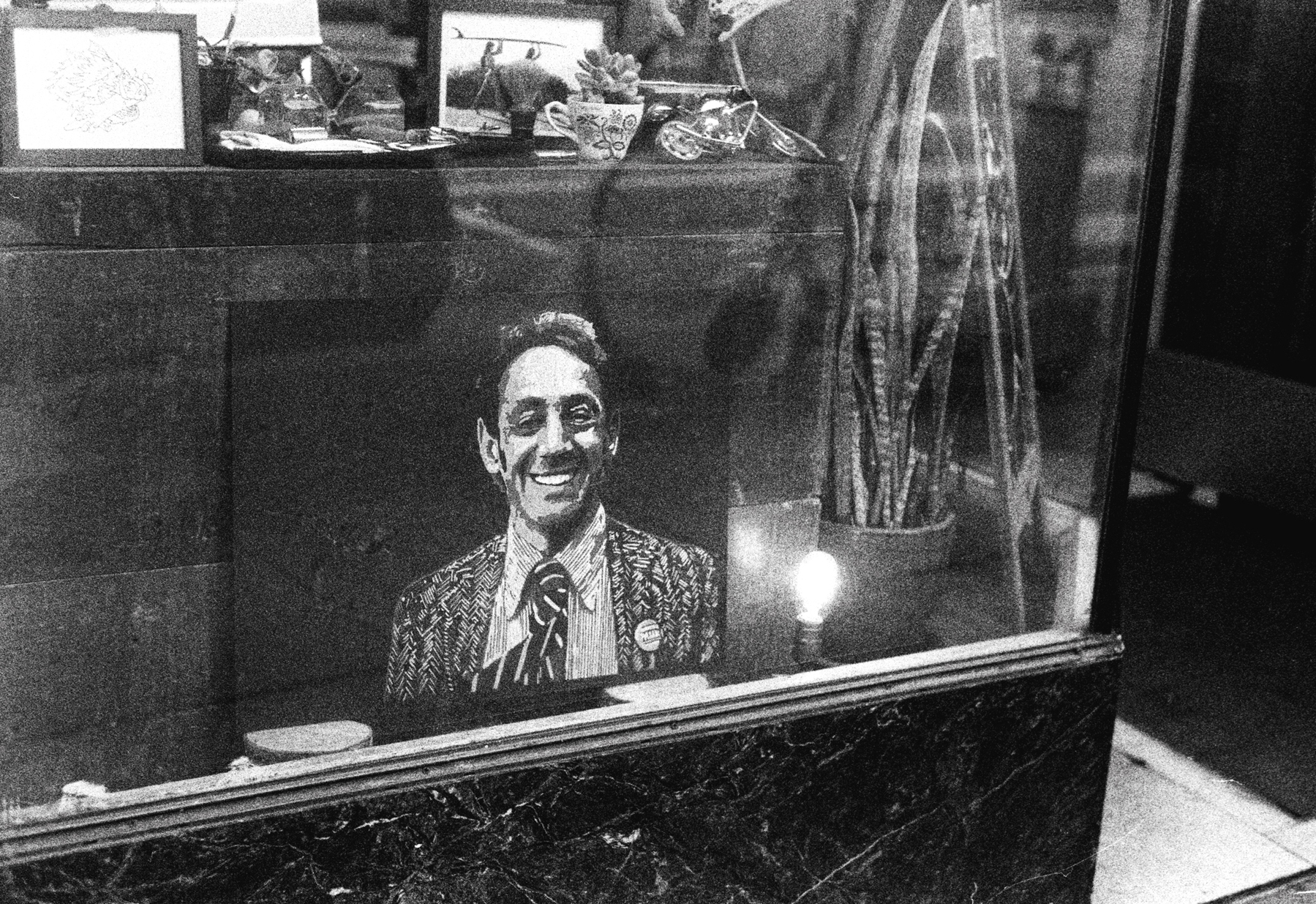 a scan of a black and white photo showing artwork featuring Harvey Milk the former gay politician of San Francisco who was assassinated a few decades ago. It sits in the window of a barber shop