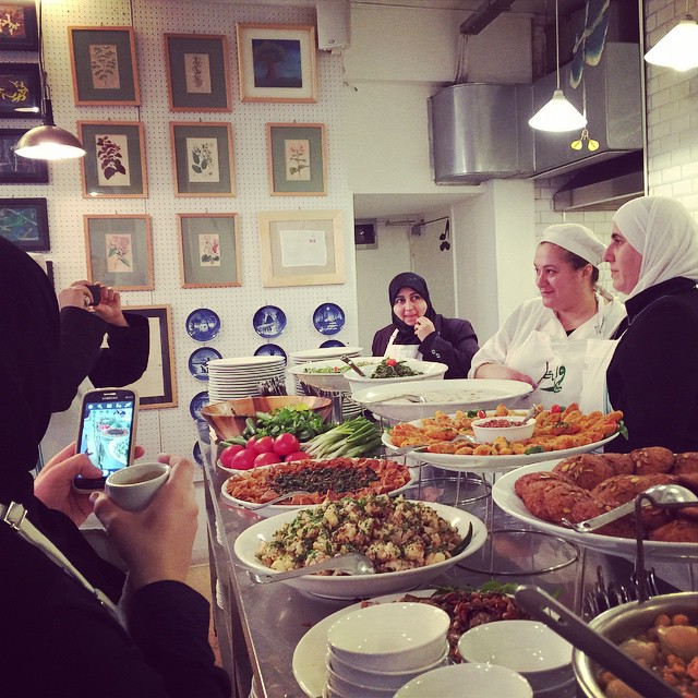 Some female chefs having their photos taken from behind many plates of Syrian food