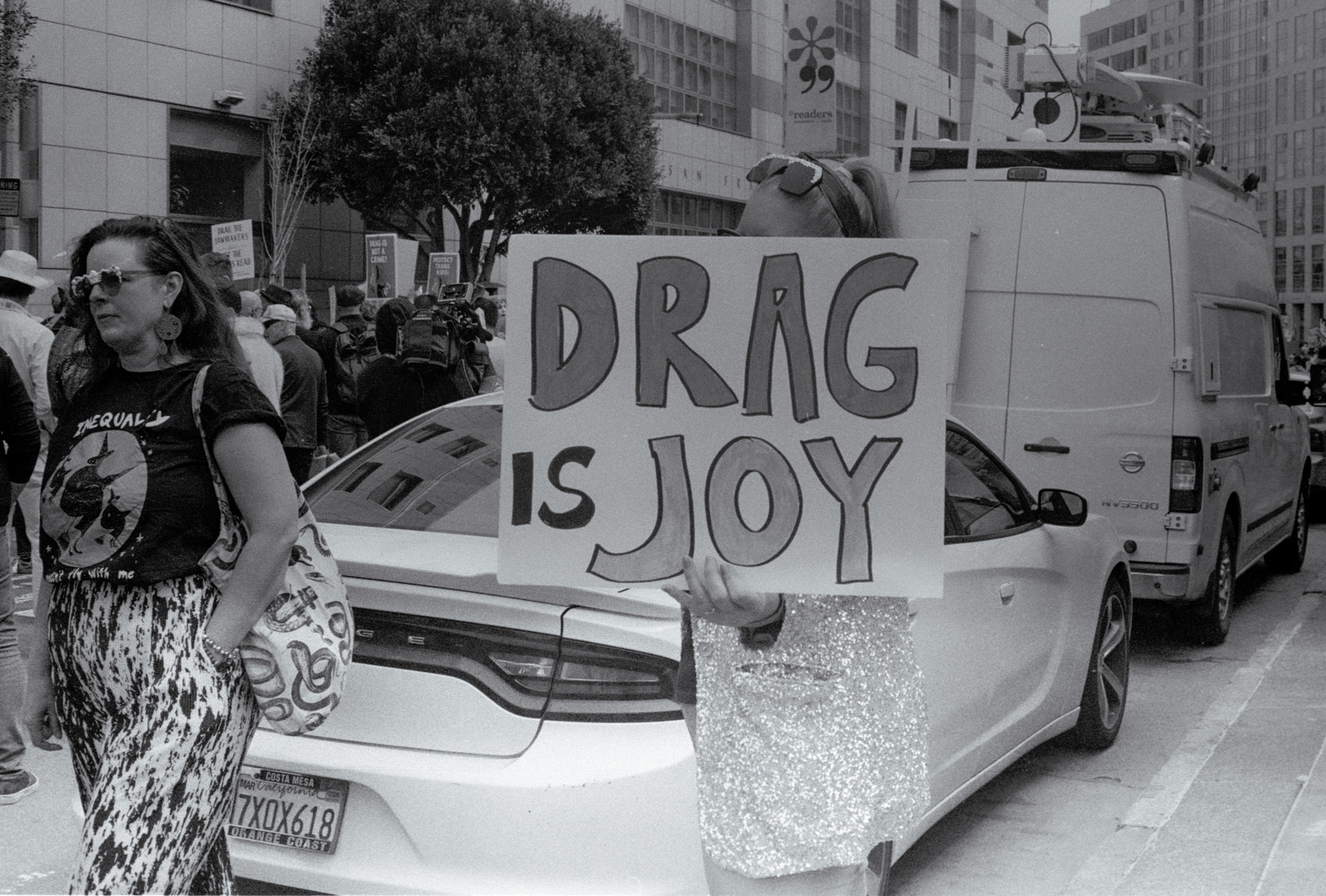 a scan of a black and white photo showing someone holding a sign that says Drag is Joy 