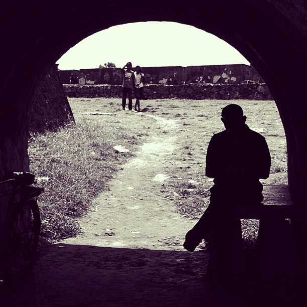 A black and white photo of a man sitting at a bench under a circular arch