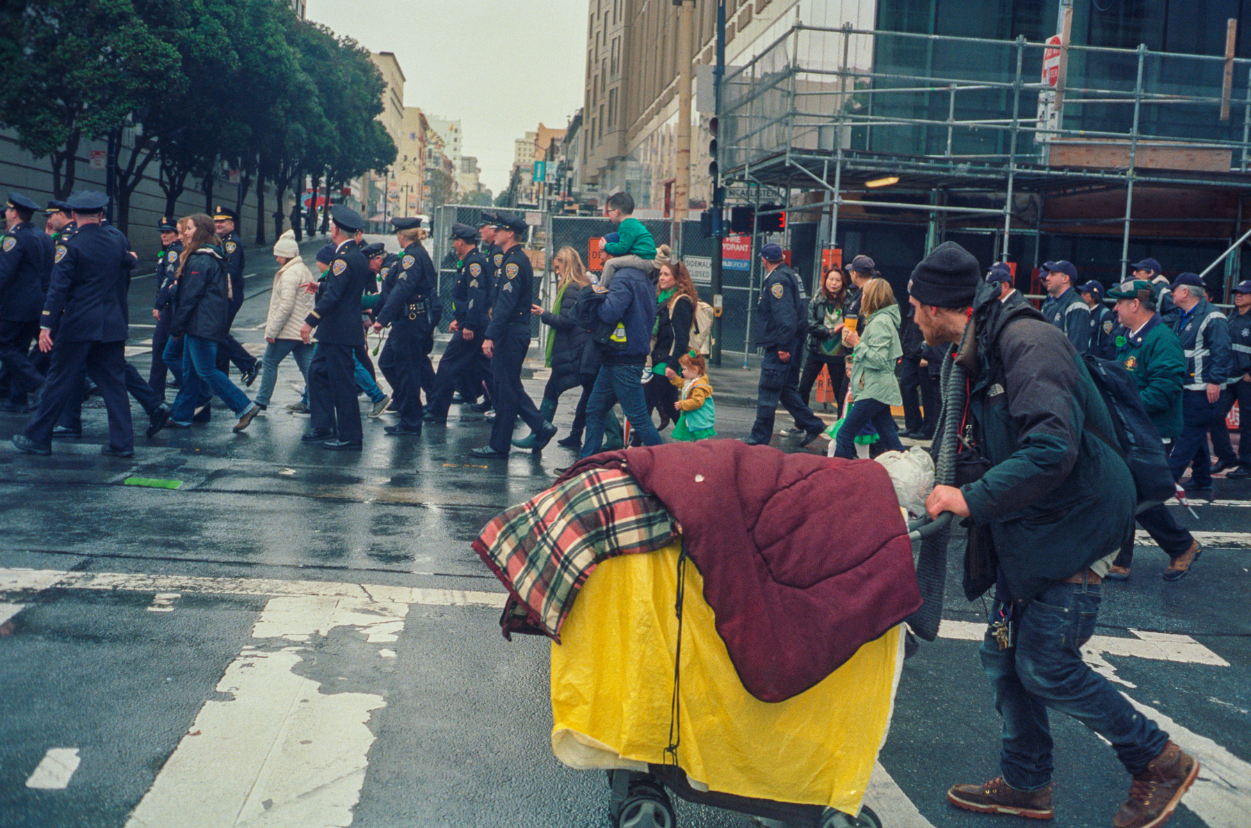 a scan of a color photograph of a homeless person walking by a large contingent of police in San Francisco who are attending St Patricks Day festivities