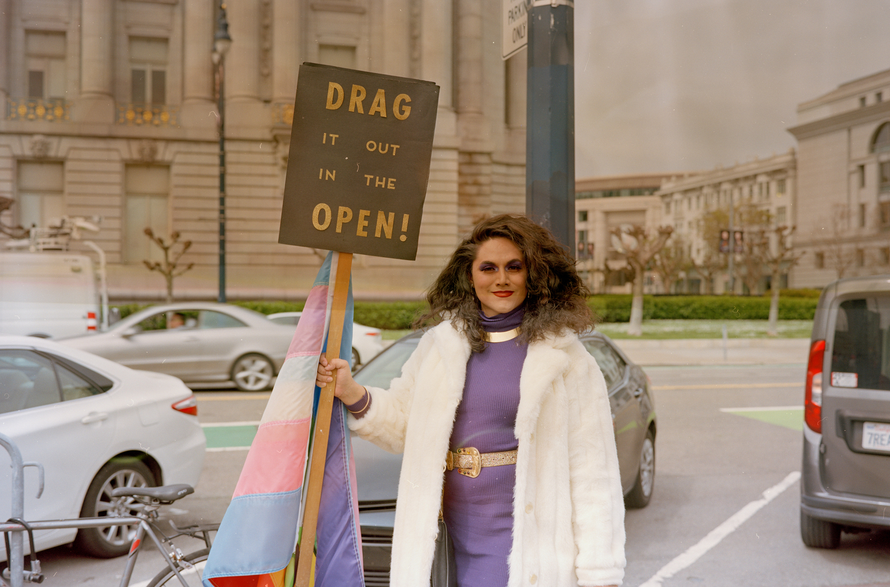 a scan of a color photo of a person holding a sign that says Drag it out in the open