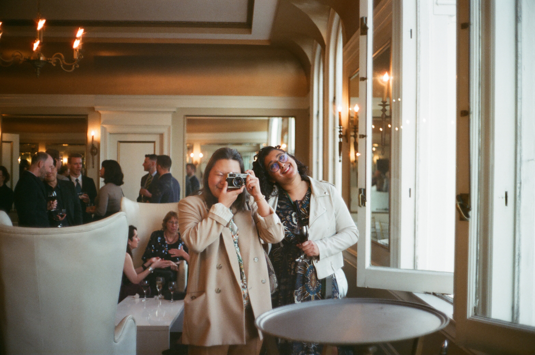 a color photograph of a queer couple taking a photo in a mirror with a film camera in San Francisco in a gala-like setting with formal attire
