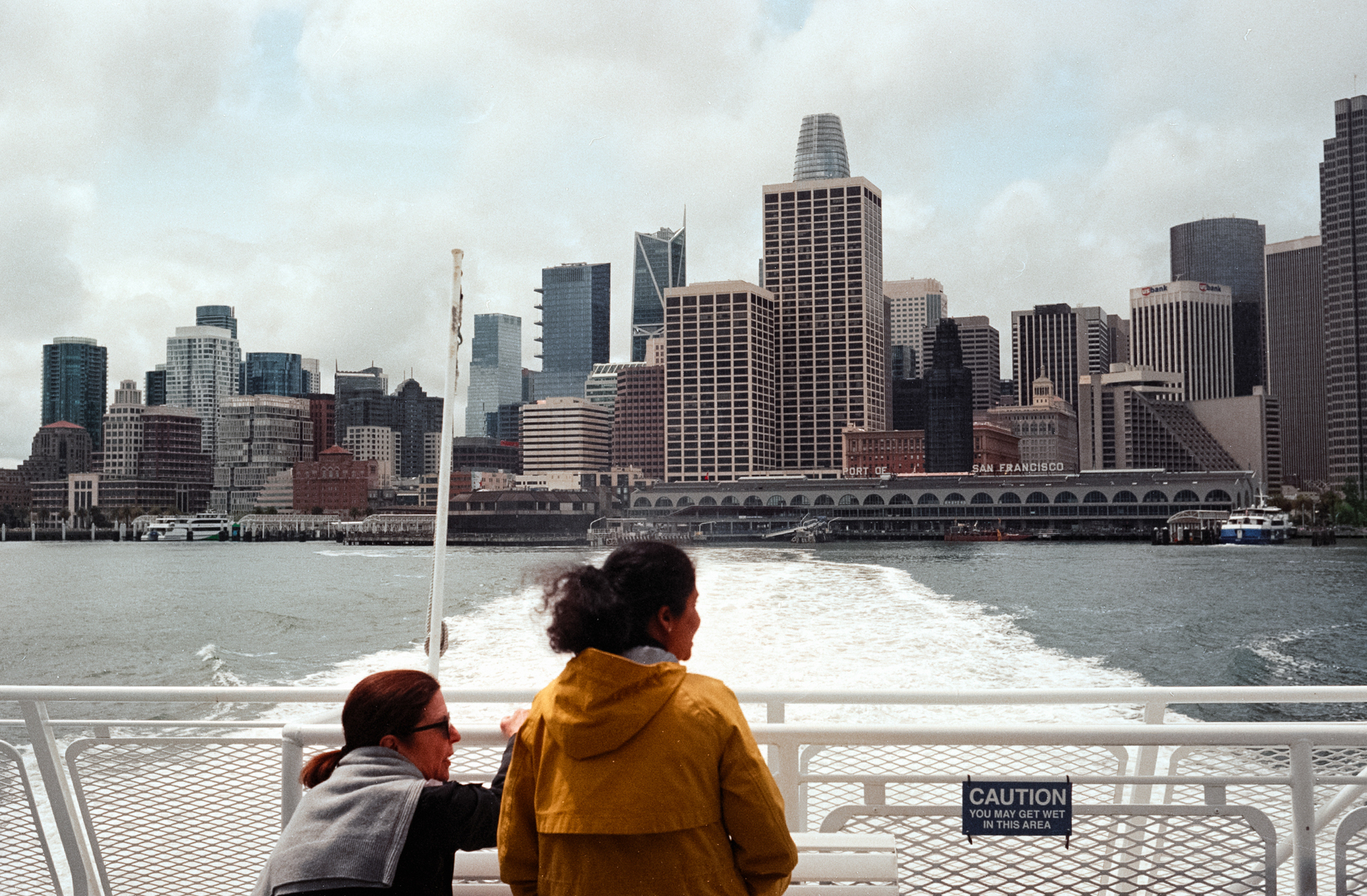 A scan of a color photograph of two women looking at San Francisco ferry building as a ferry pulls away from the harbor