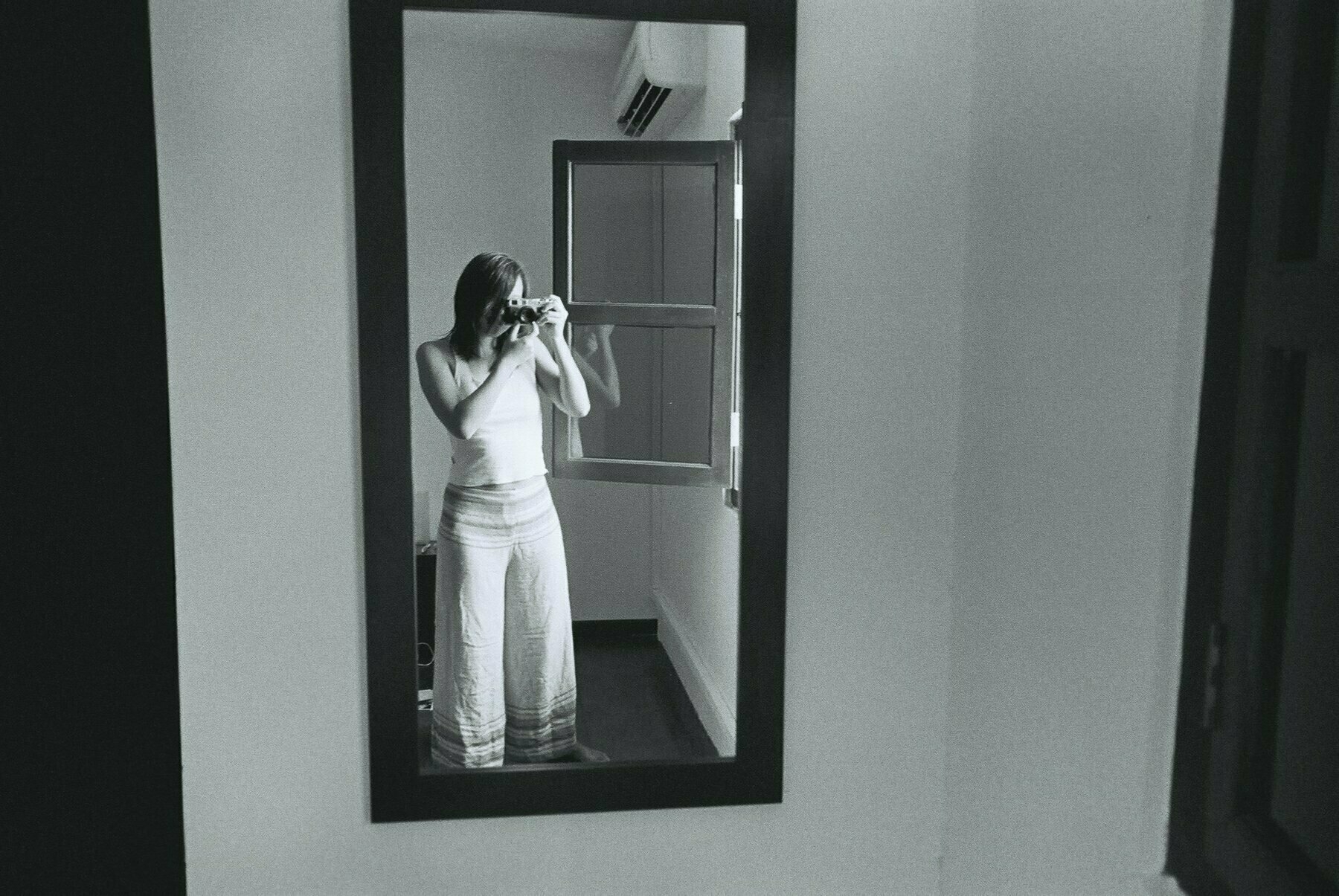 a black and white photograph of a person taking a photo of themselves in the mirror in Melaka, Malaysia