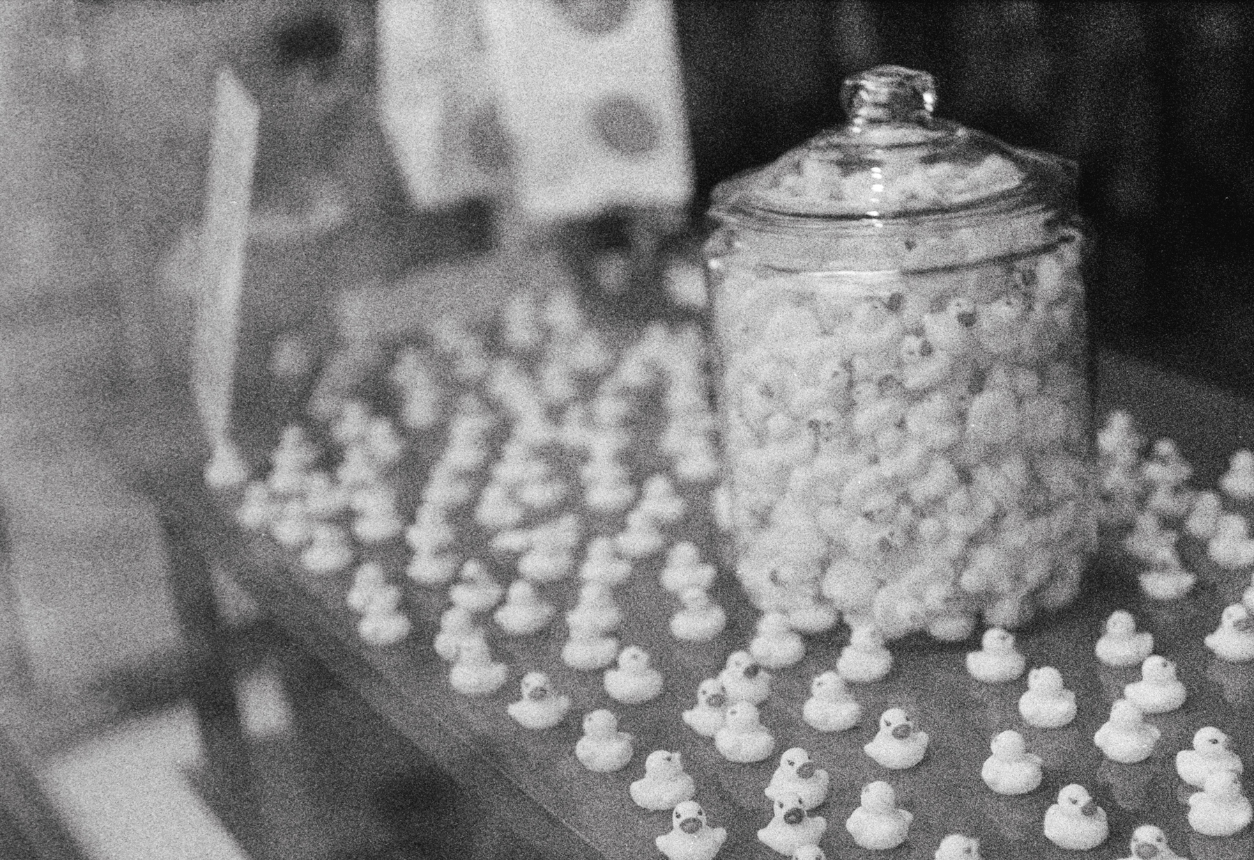 a scan of a black and white photo showing a bunch of rubber ducks on a table inside a glass jar sitting on a window