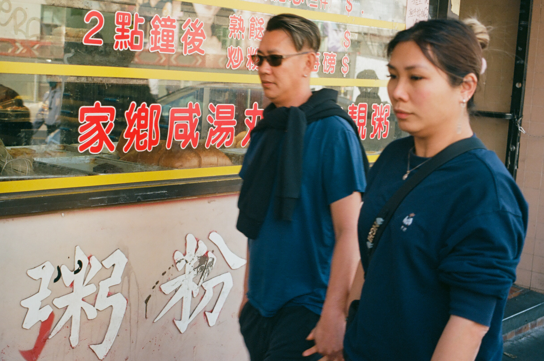 A color photograph of a Chinese restaurant with Chinese text on the windows, and an Asian couple walking in front of it