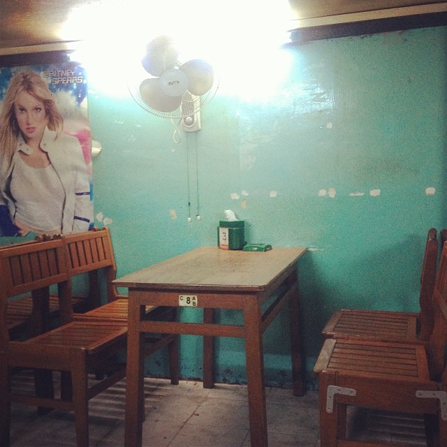 a photo of the insides of a Burmese restaurant with blue pastel walls and wooden chairs and tables and a very old photo of Britney Spears on the wall