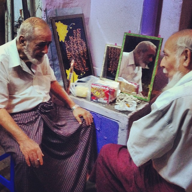 a photo of two senior Burmese Indian gentlemen sitting on very small chairs and talking to each other