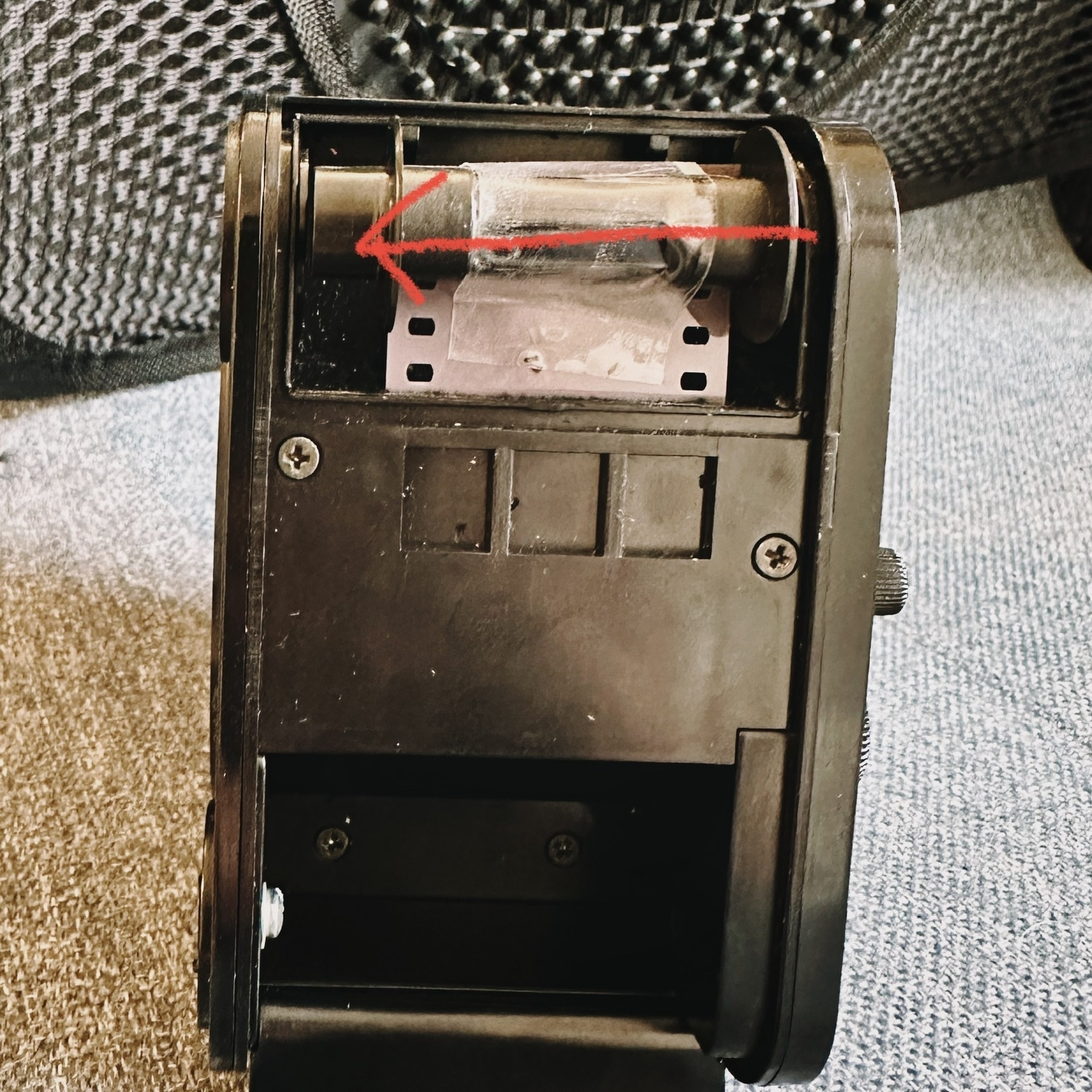 a photo of a film bulk loader showing the film coming out of the loader, with a red arrow showing the direction of the film cassette