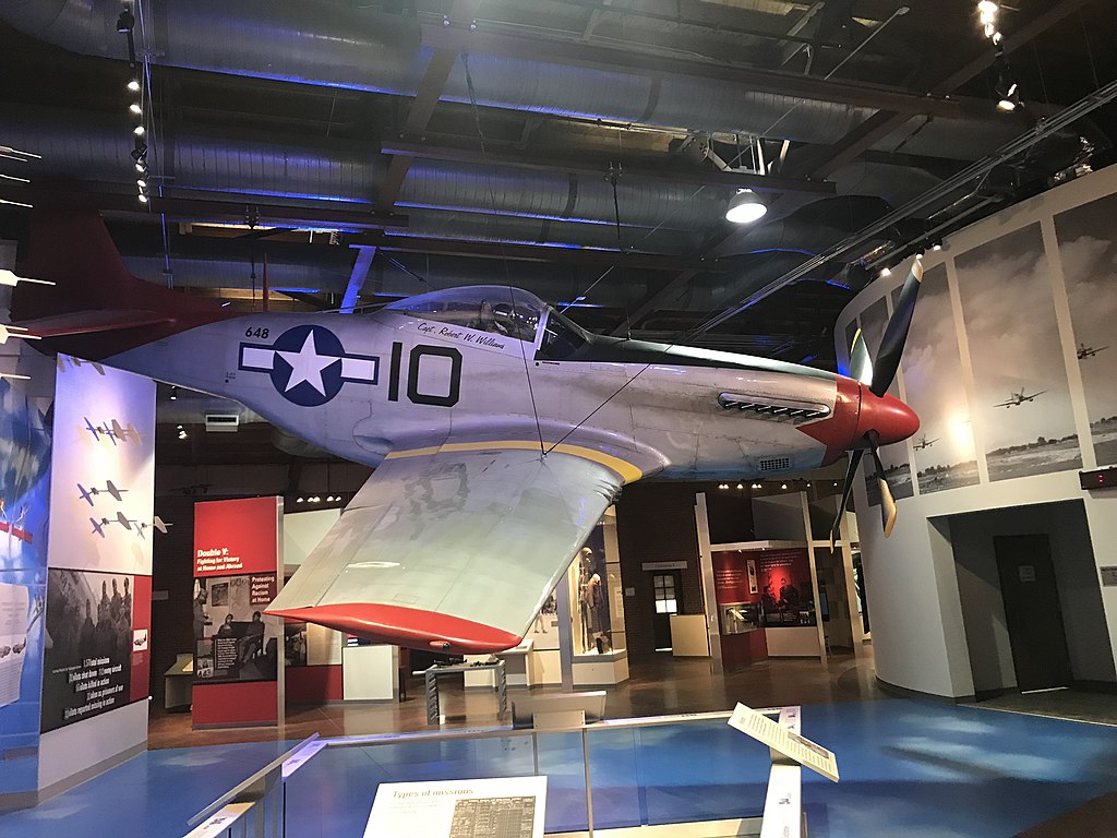 A red-tail P-51 Mustang suspended from the ceiling in a museum.