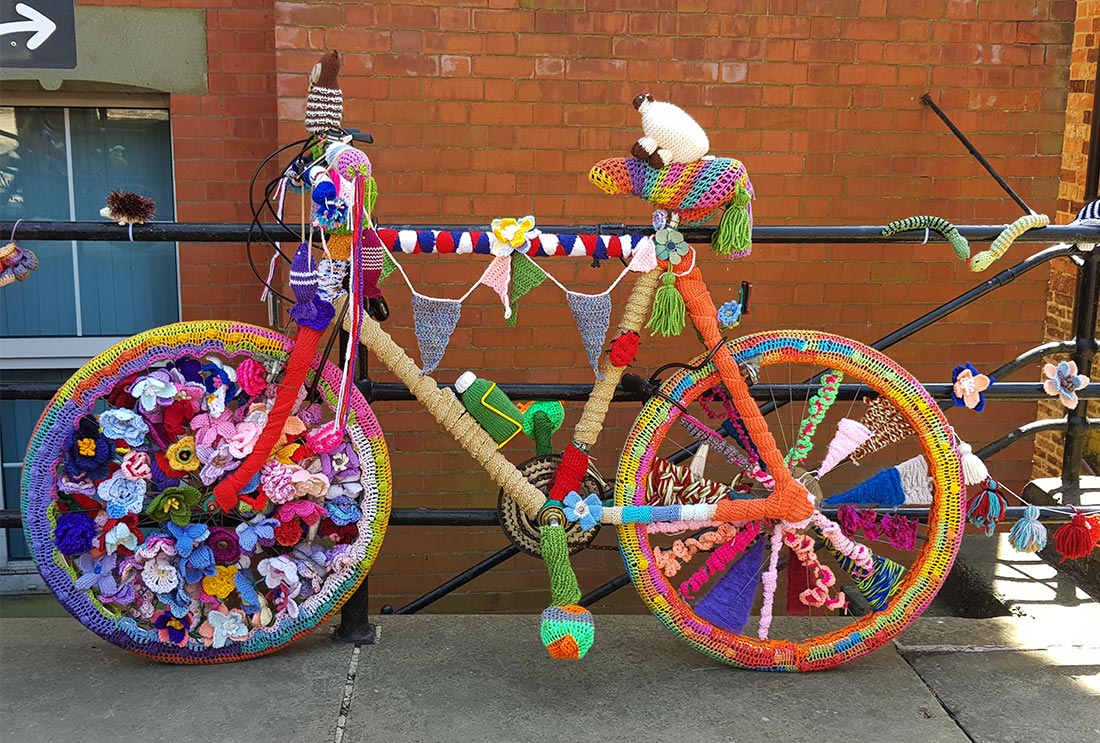 A bicycle leaning against a wall, competely covered in knitting and crochet work.