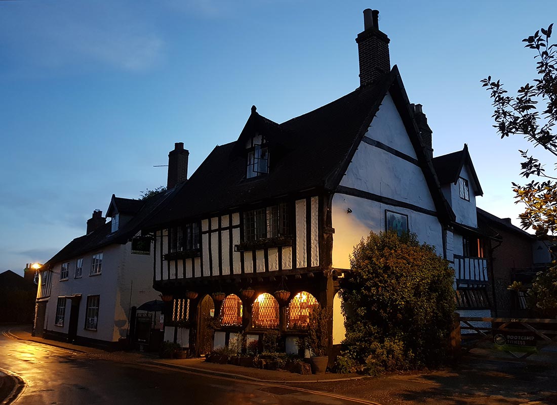 A night-time scene of the Green Dragon pub in Wymondham, Norfolk, UK, its windows lit from within and glowing invitingly.