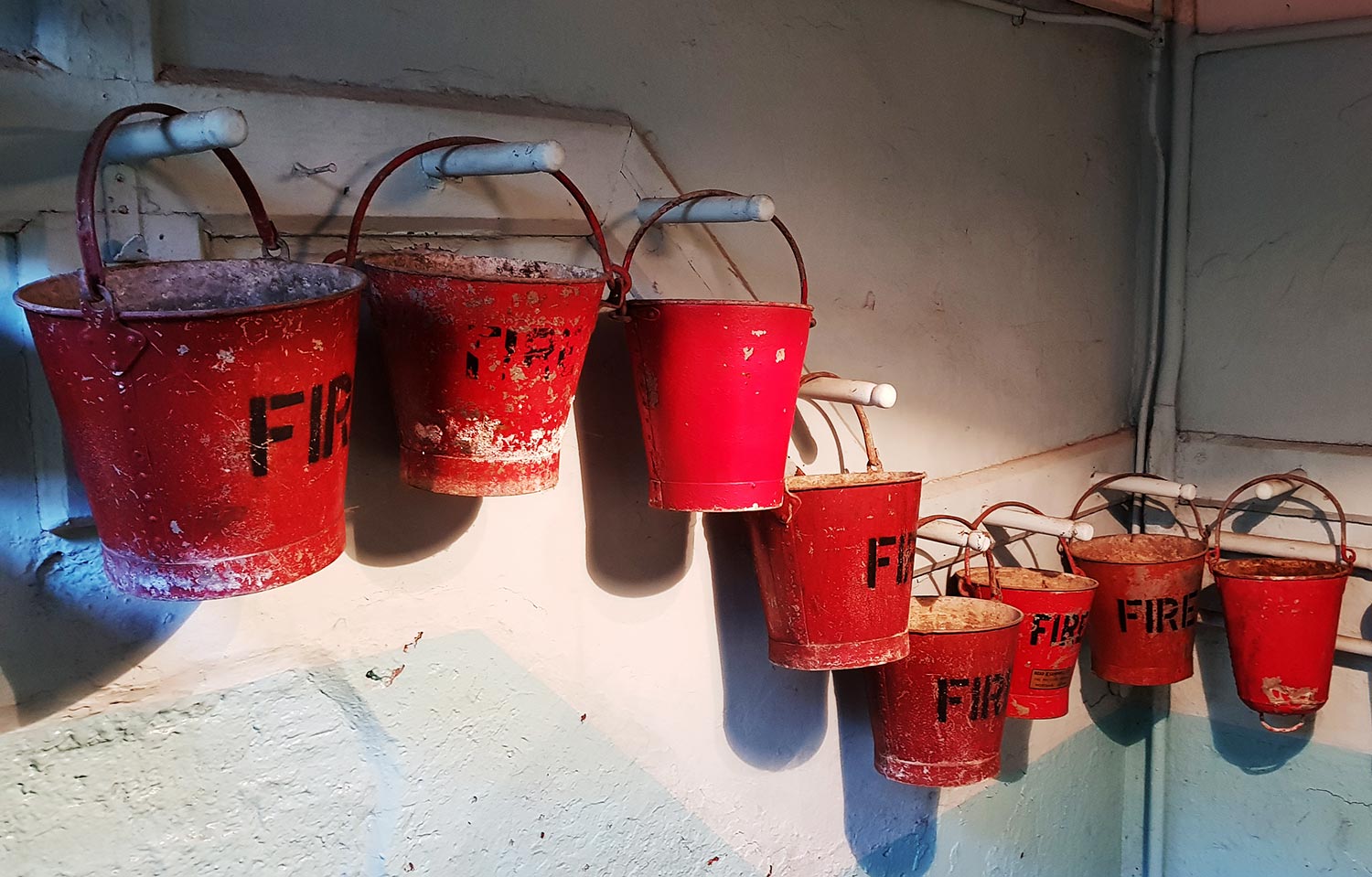 A row of old red fire buckets hanging on the wall in a stairwell