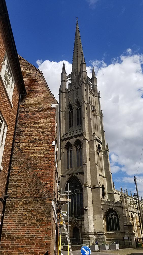The steeple of St James church in Louth, UK, photographed from street level. Part of a red brick Georgian house can be seen on the left side; there is a lot of perspective distortion so the buildings appear to lean in.