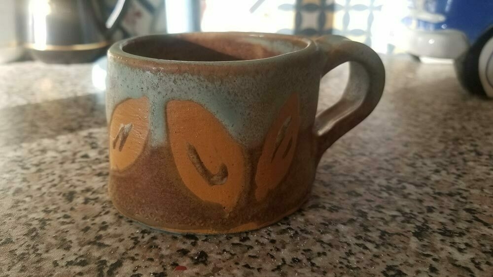 Handmade chunky pottery mug in shades of yellow ochre and celadon green, decorated around with yellow abstract leaf shapes 