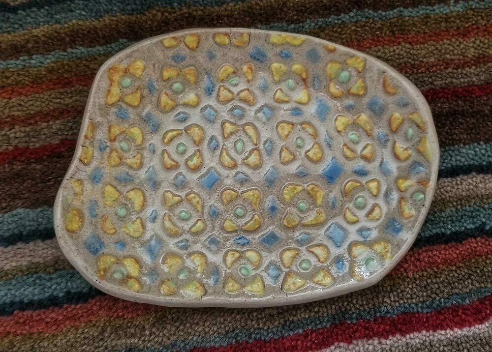 A small handmade pottery dish decorated with a painted floral abstract pattern, with a rather retro 1960s vibe.