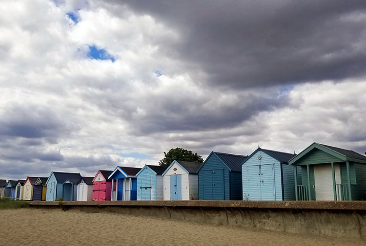 A row of colourful painted beach huts on the edge of the sand beneath a dark, stormy sky