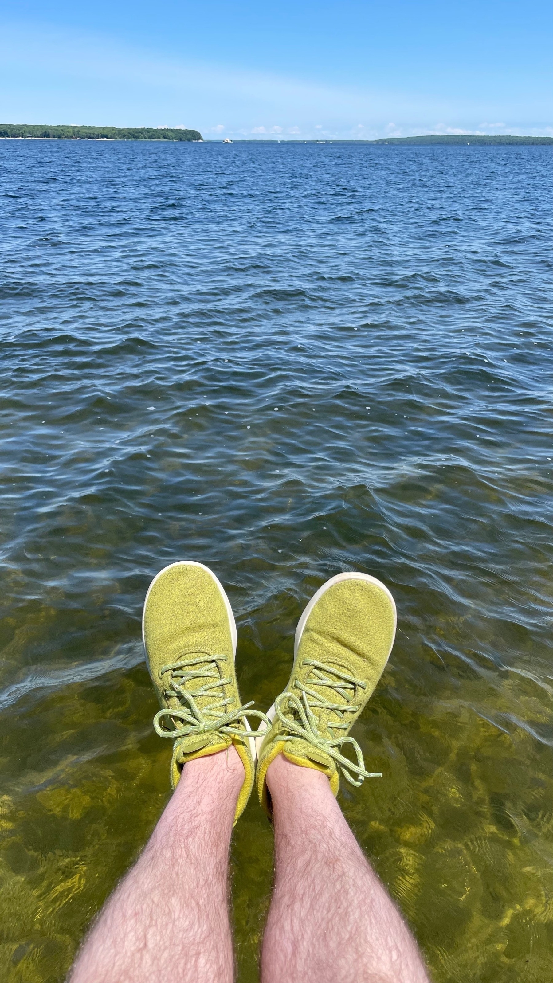 Selfie of my feet in loud green wool shoes over the green and blue water of Georgian Bay. Blue sky and boats in the distance.