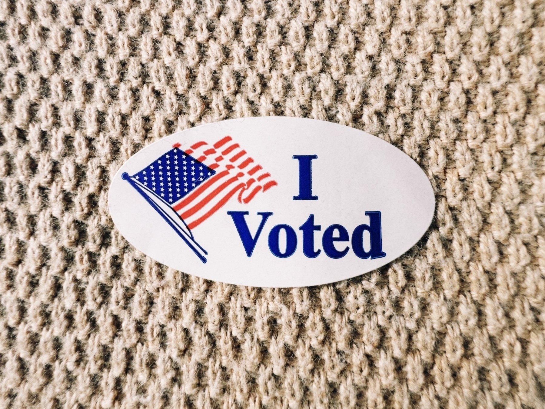 “I Voted” sticker with American flag, stuck on my tan knitted sweater.