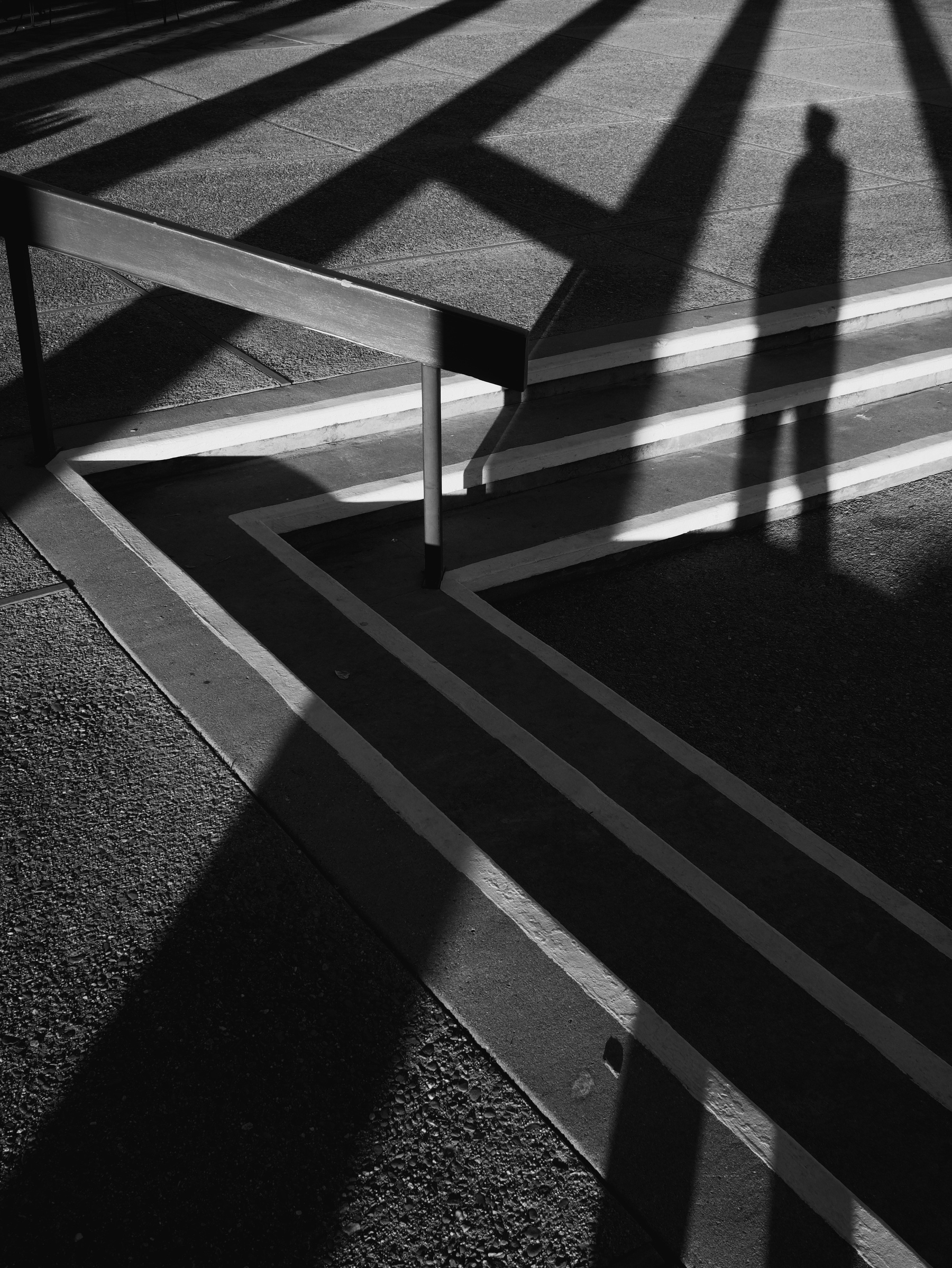 Black and white photo. Shadows cross over a set of stairs that are angled to look like three “less-than” signs.