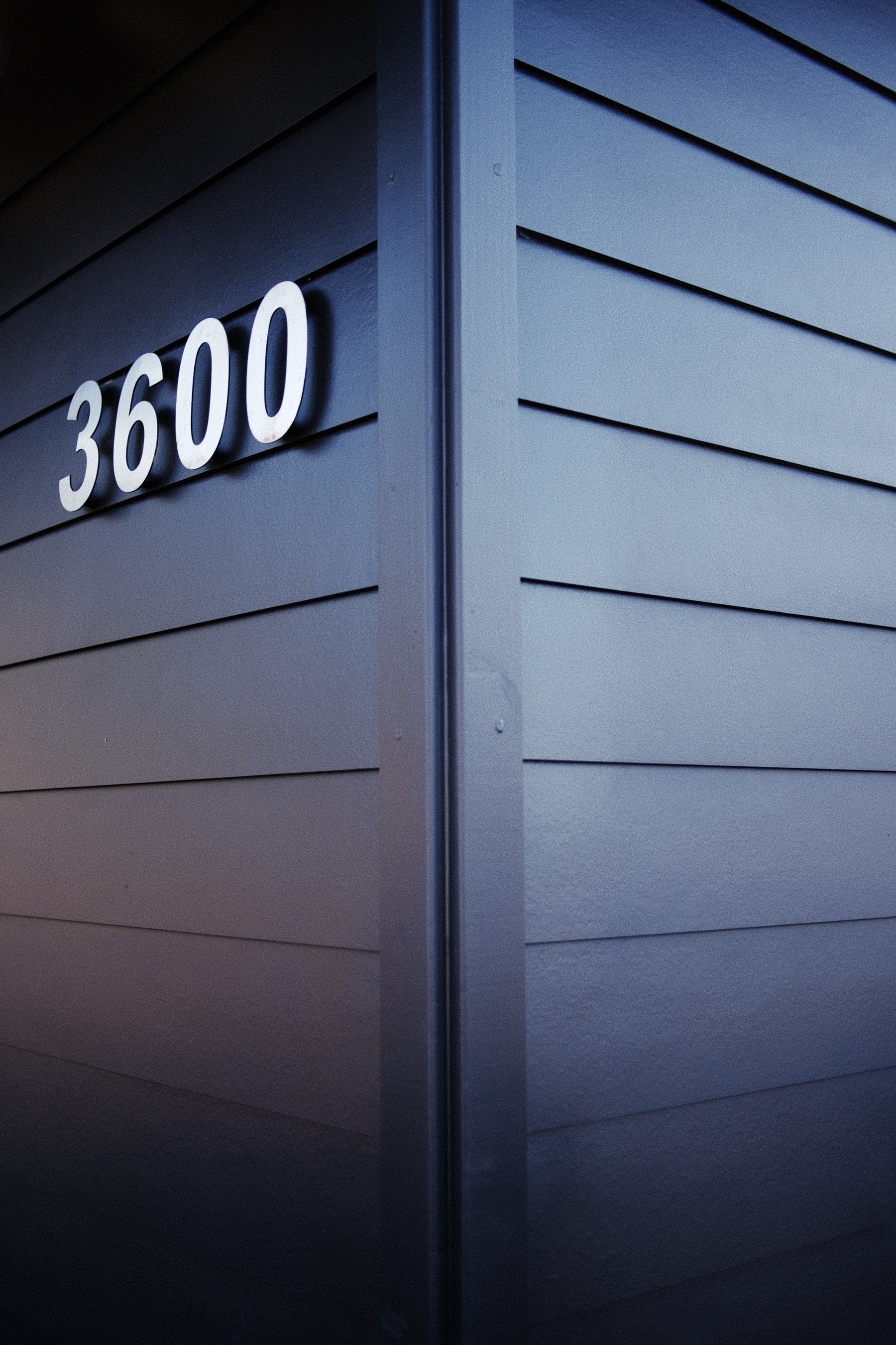 Photo of a corner of a building. Blue and orange tones. On the left side, the numbers 3600 are mounted on the wall.