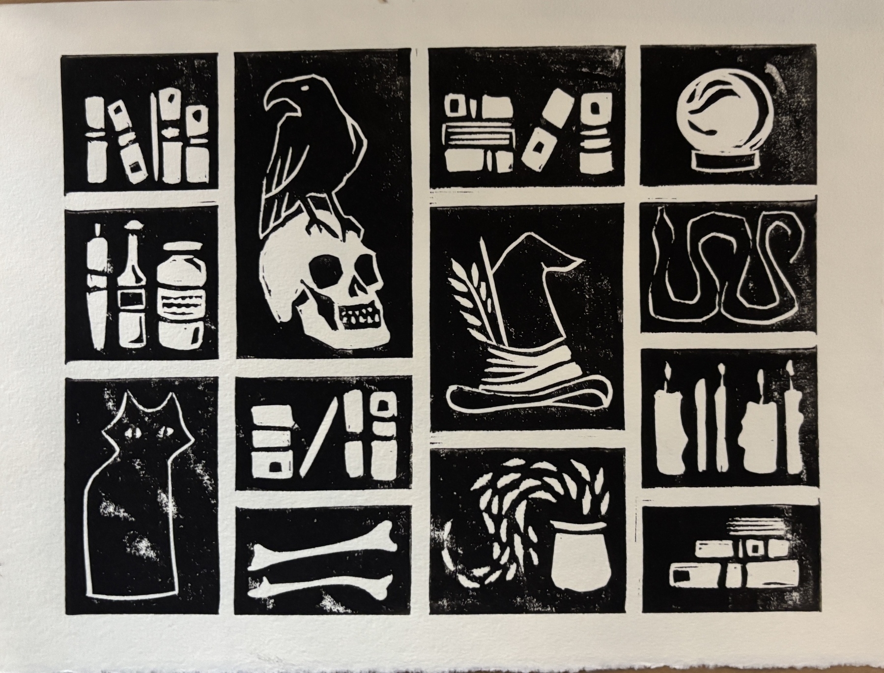 Black and white print of a bento box with a black cat, skull and raven, candles, bones, potions, a snake, a crystal ball, and books