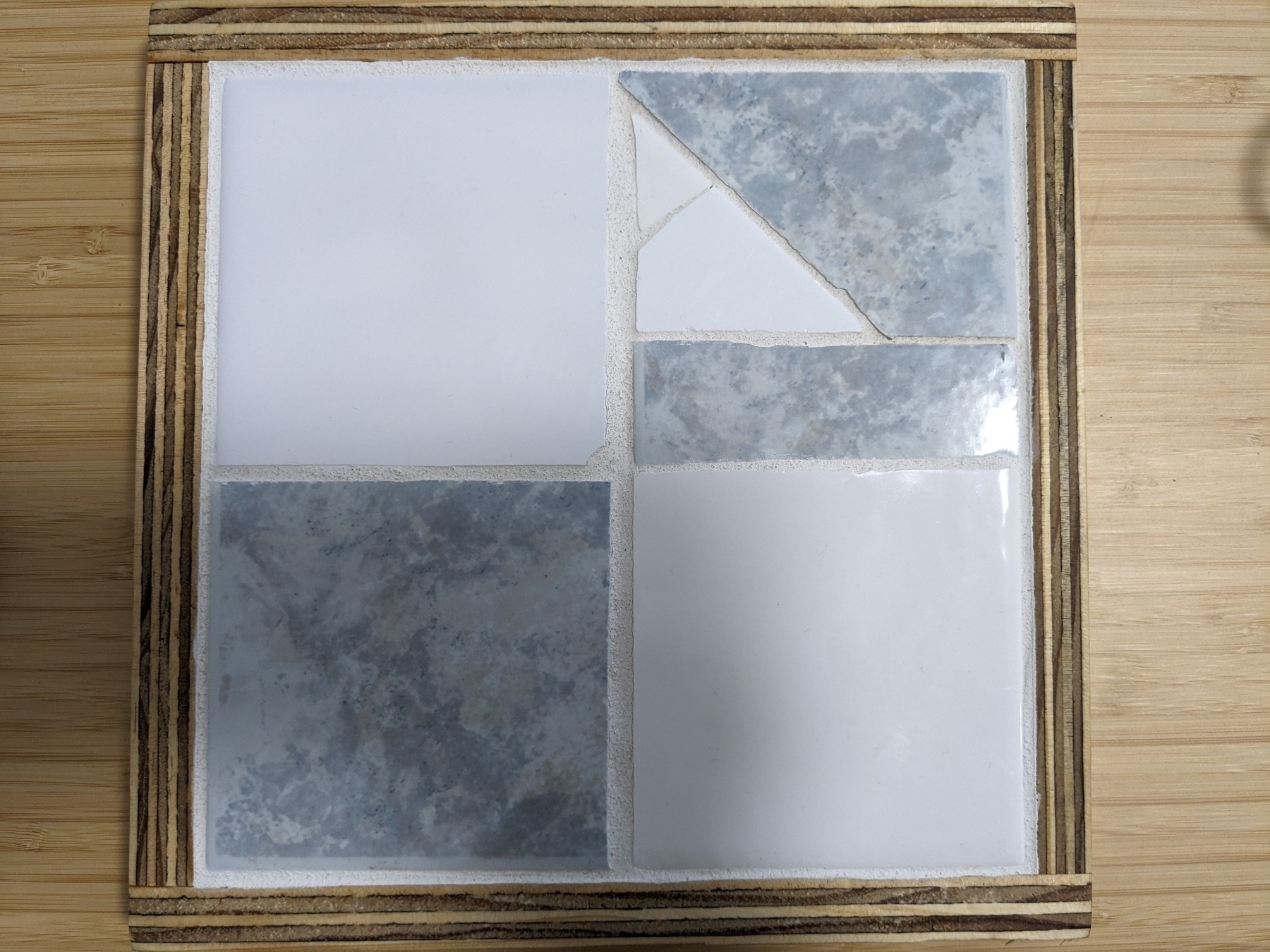 Wooden frame with four square tiles, two blue and two white, glued and grouted inside. The fourth tile is made of 4 shattered pieces. 