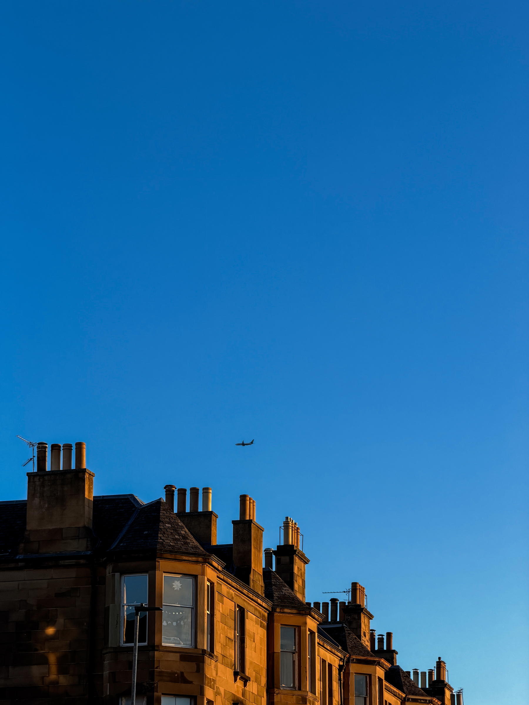 A row of tenement flats in golden light with an airplane in the distance