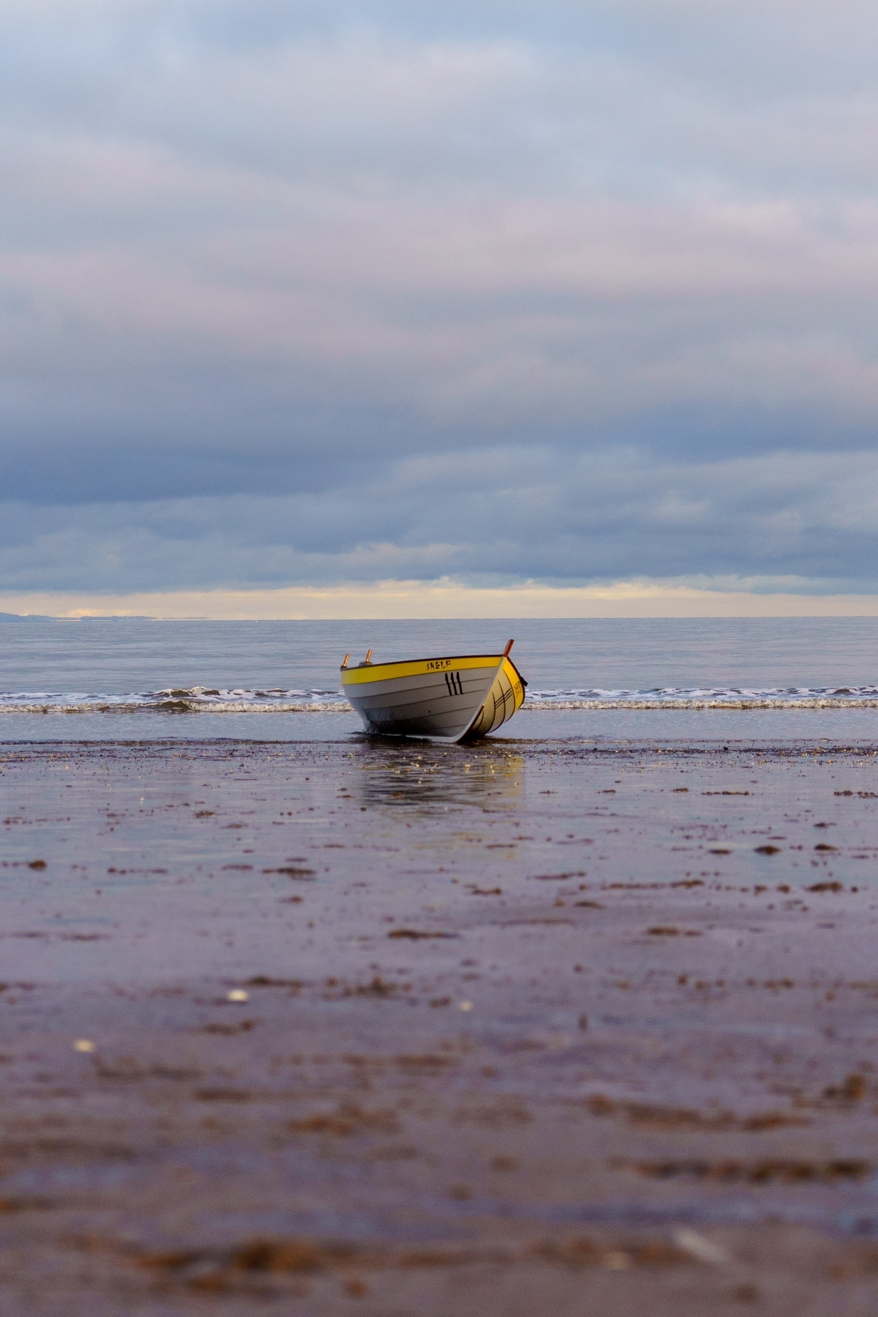 A grey boat with a yellow stripe along the top "Skelf" on a beach