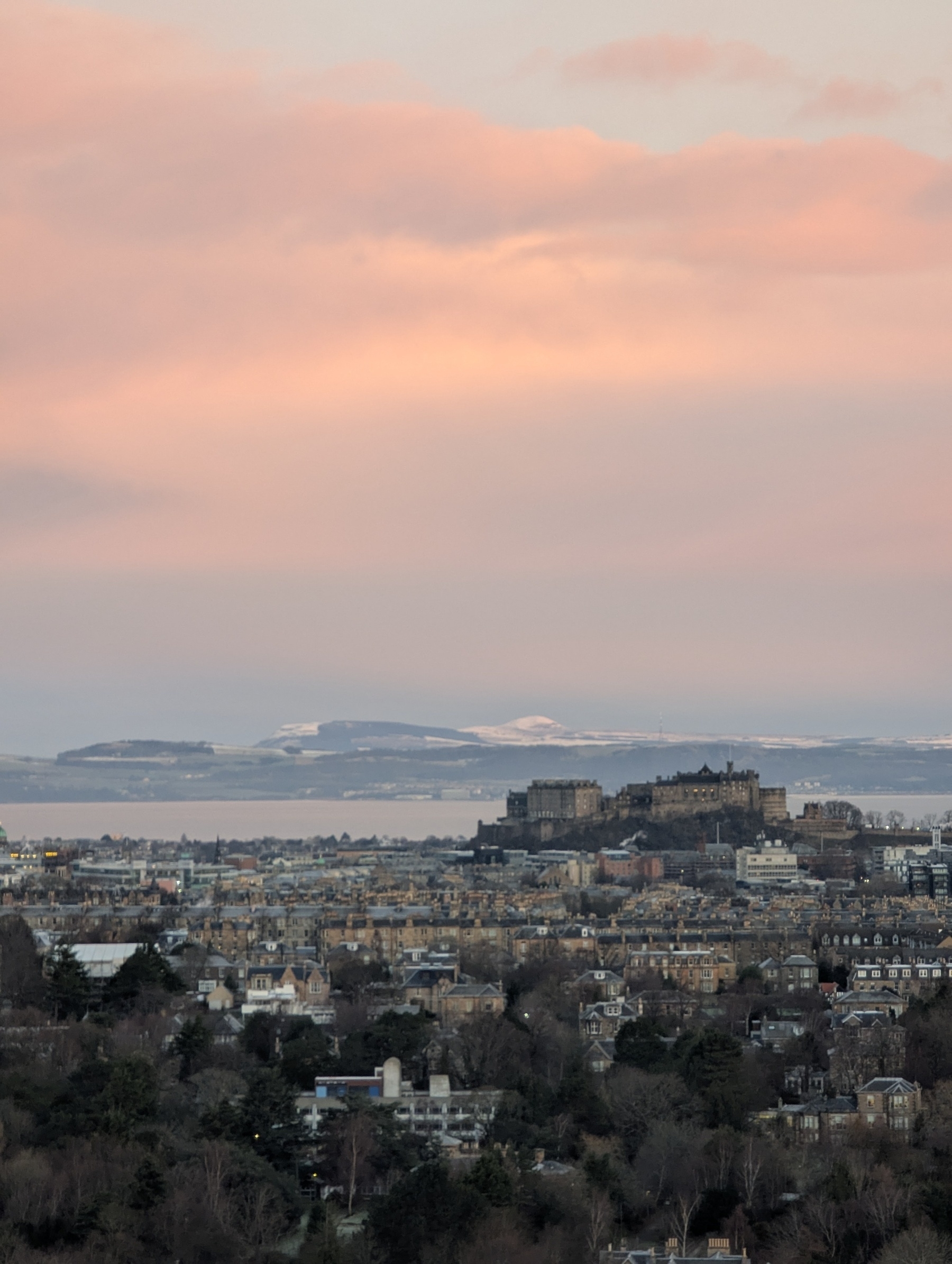 Edinburgh castle in the distance in front of snowy hills and a pink sky