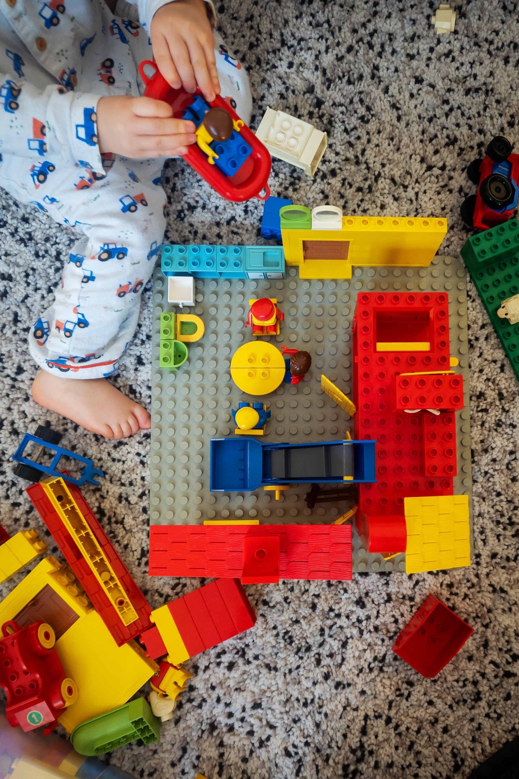 Top down view of our wee guy playing with Duplo blocks (house on a gray board)