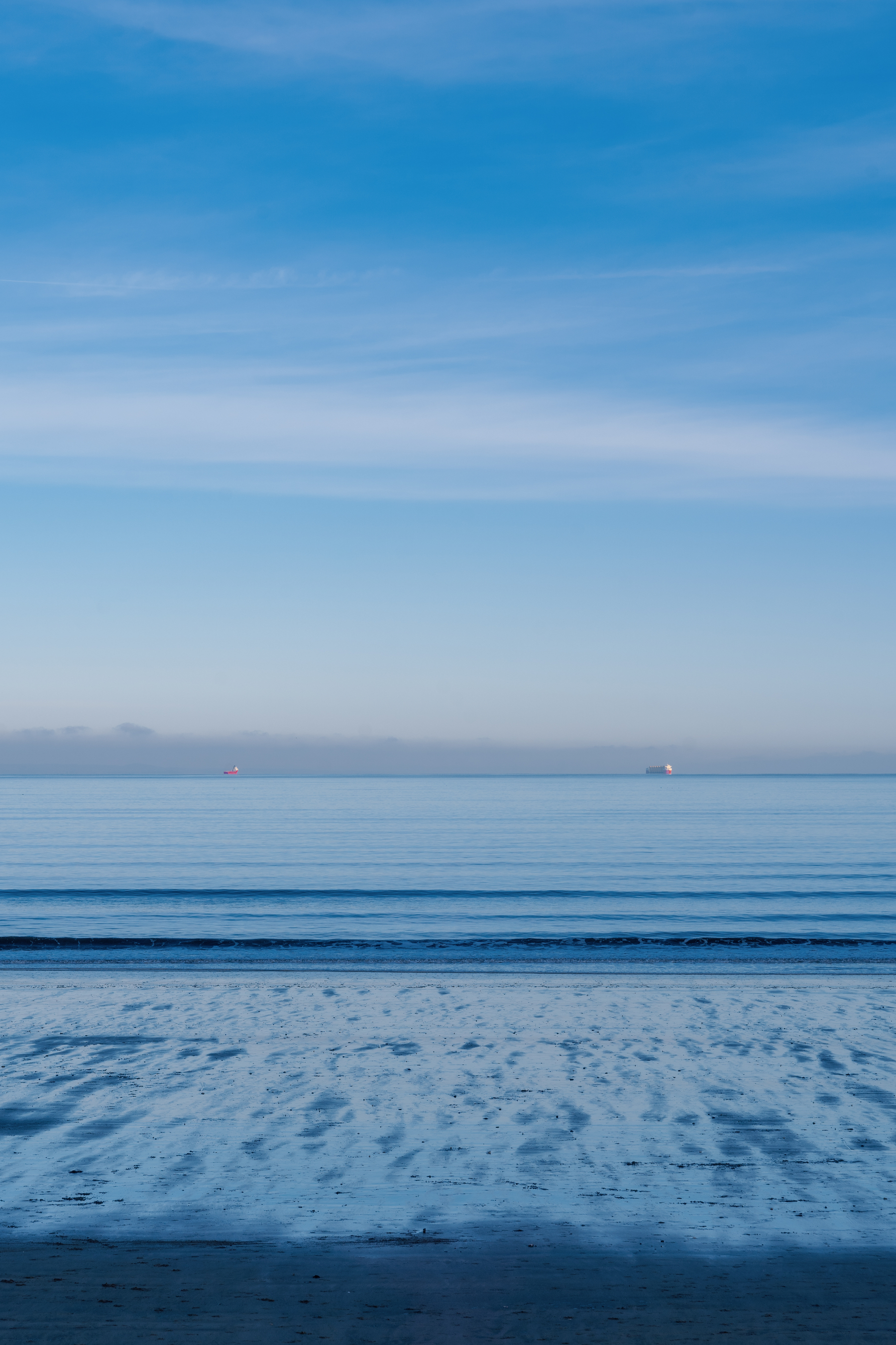 A blue view from the beach with two red ships in the far distance 