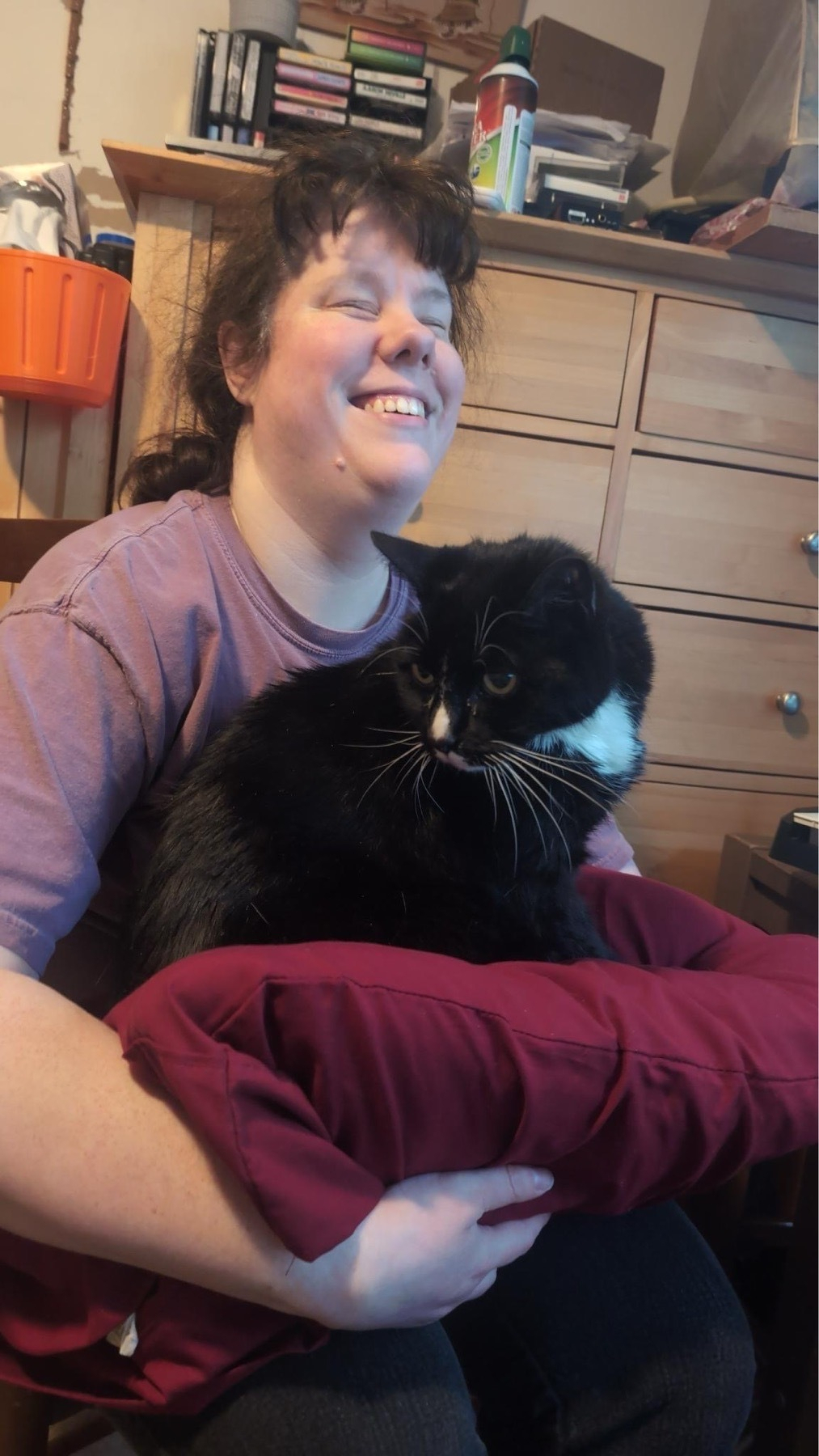 This is me smiling with a cat on my lap. I’m holding him on a cushion so that he doesn’t fall because the width of my legs doesn’t give him the room he needs to lie comfortably.