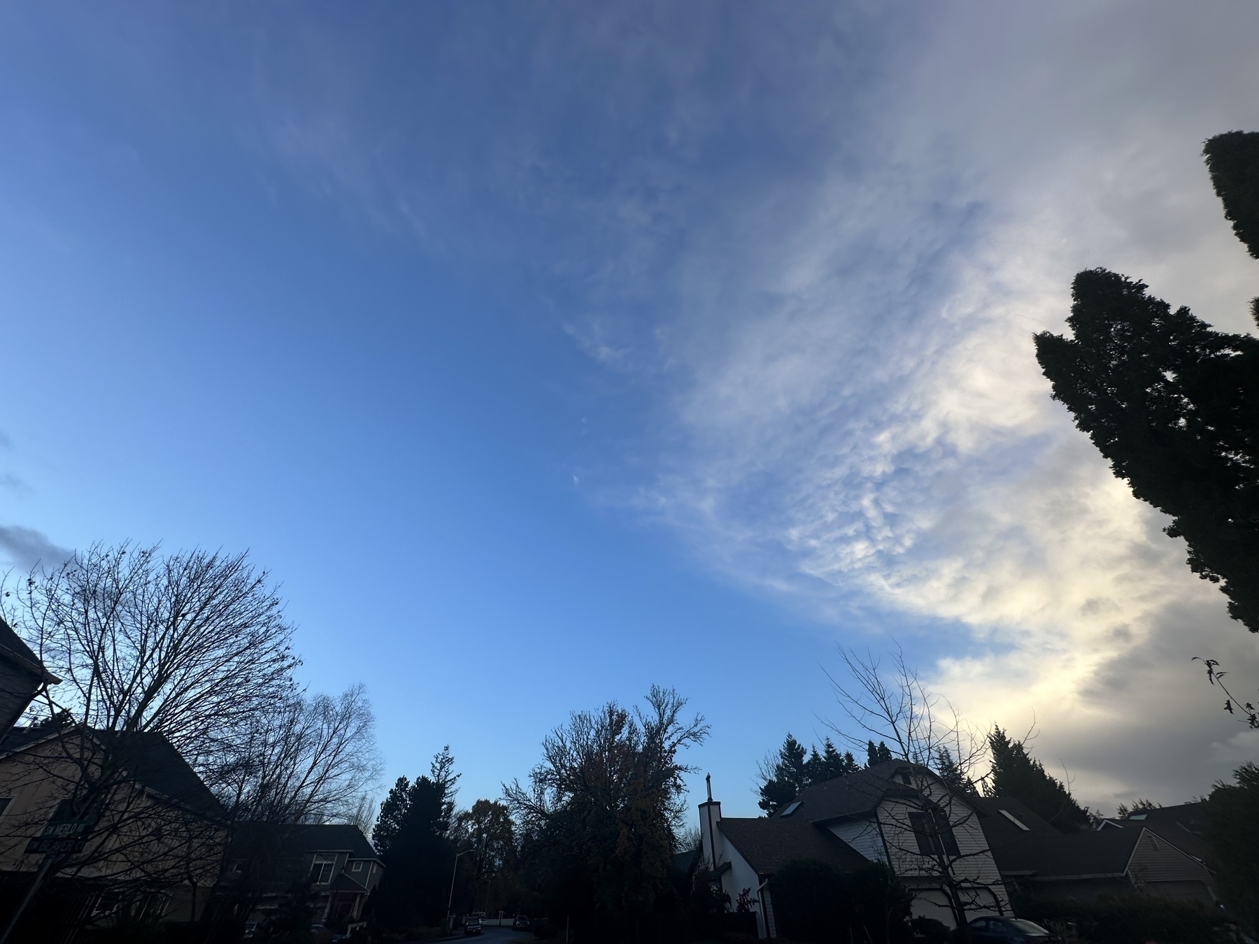 A suburban neighborhood is shown under a vast sky with a mix of blue and cloud coverage.