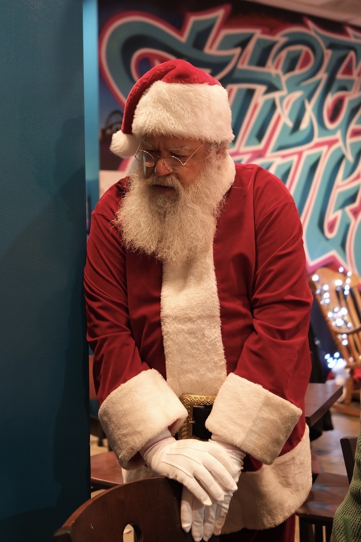 A person dressed as Santa Claus is leaning against a wall, with a graffiti-style background.