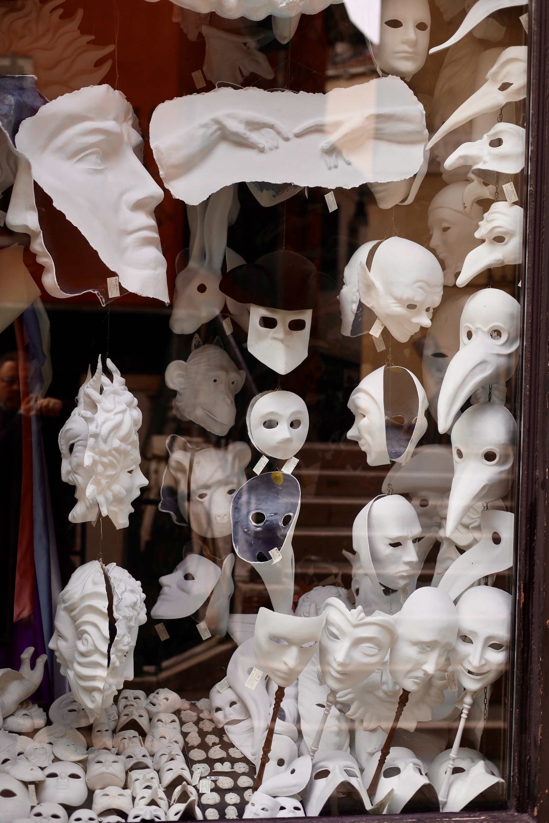 A display window is filled with various white theatrical and carnival masks of different shapes and sizes.