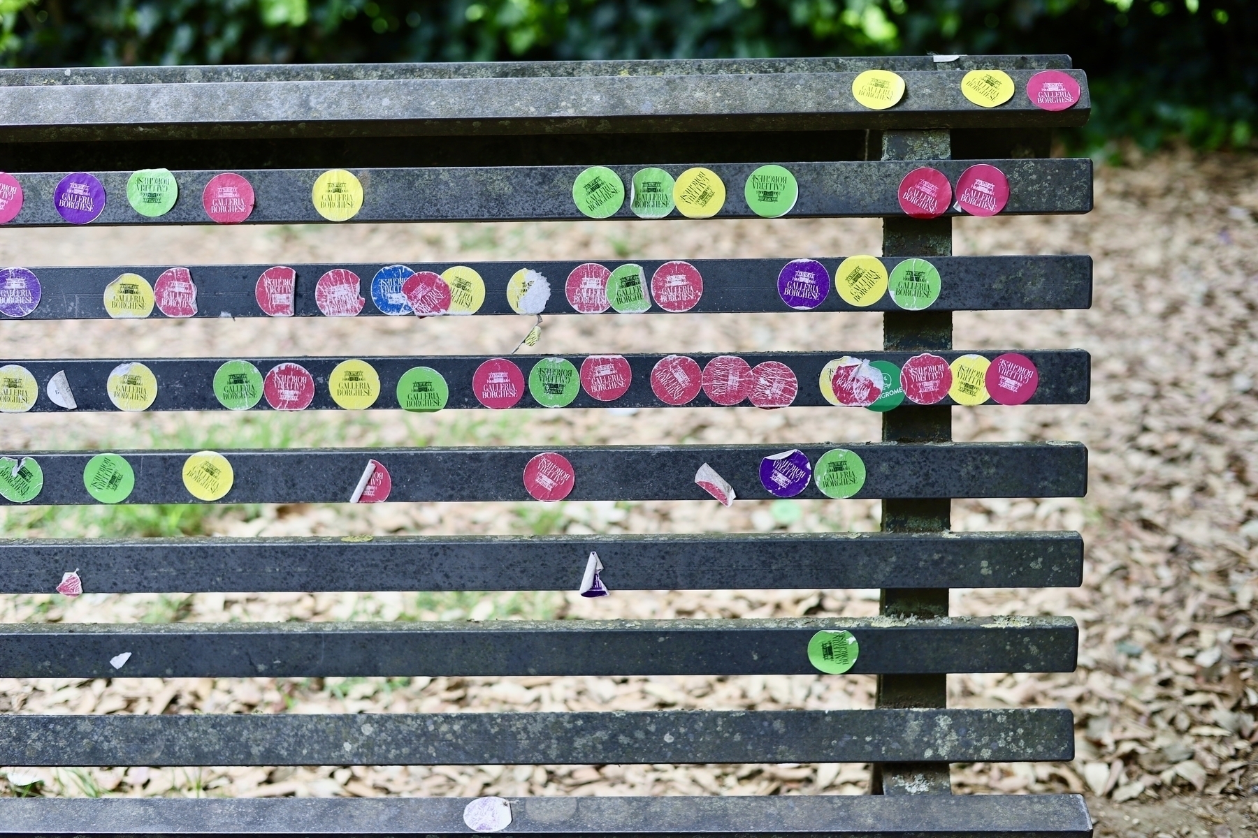 Colorful stickers are scattered across the wooden slats of an outdoor bench.