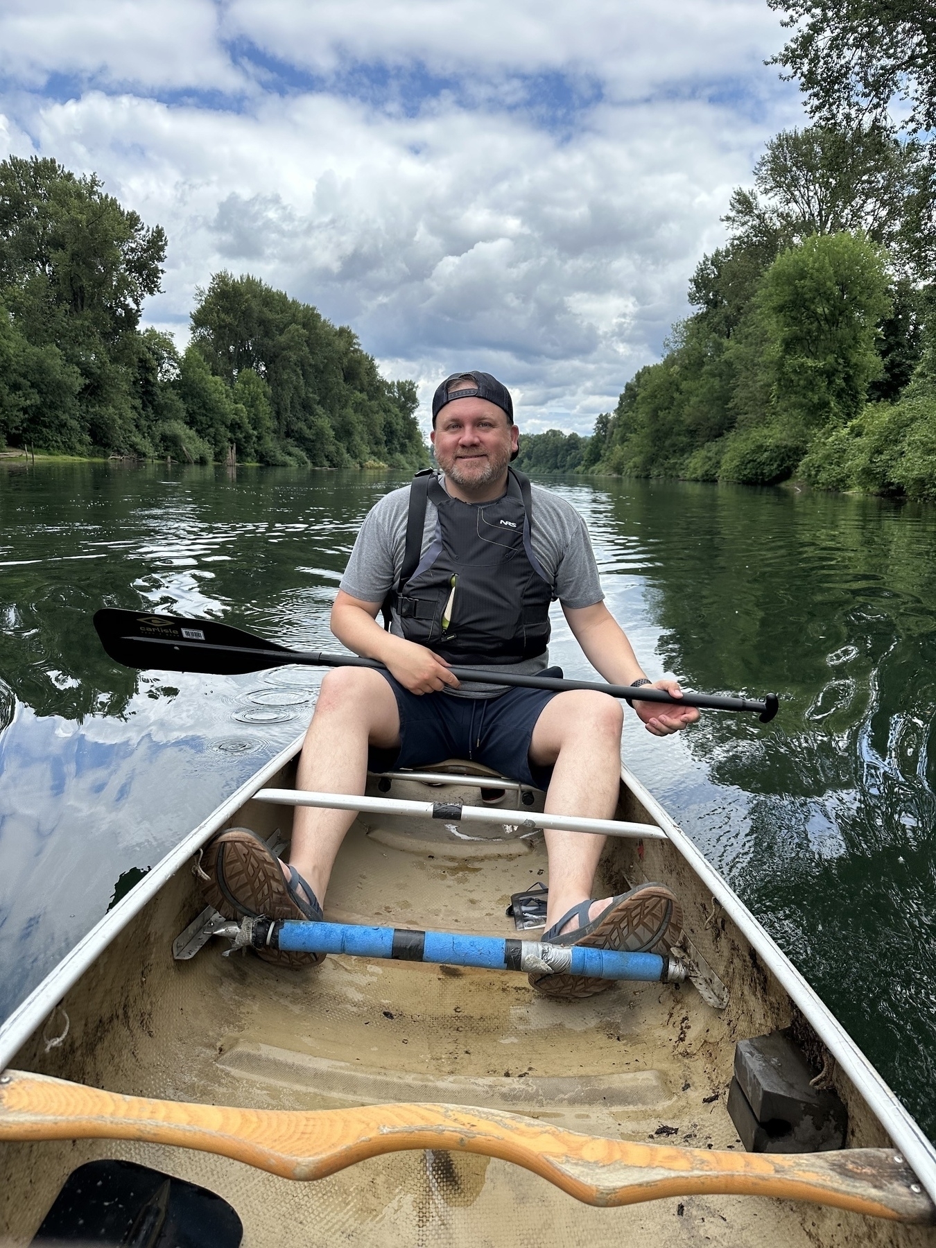 A person is sitting in a canoe paddling down a calm river surrounded by lush greenery.