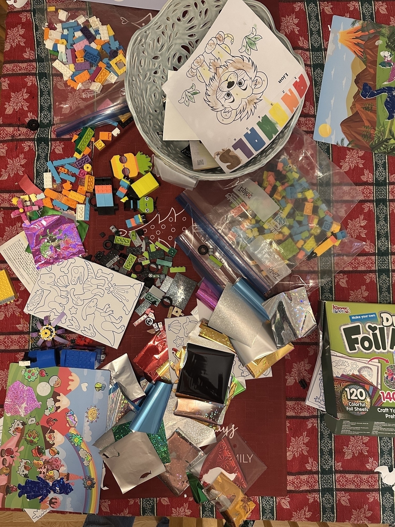 A table is covered with various art supplies, including drawings, colored paper, LEGO pieces, and a box labeled "Dazzling Foil Art."