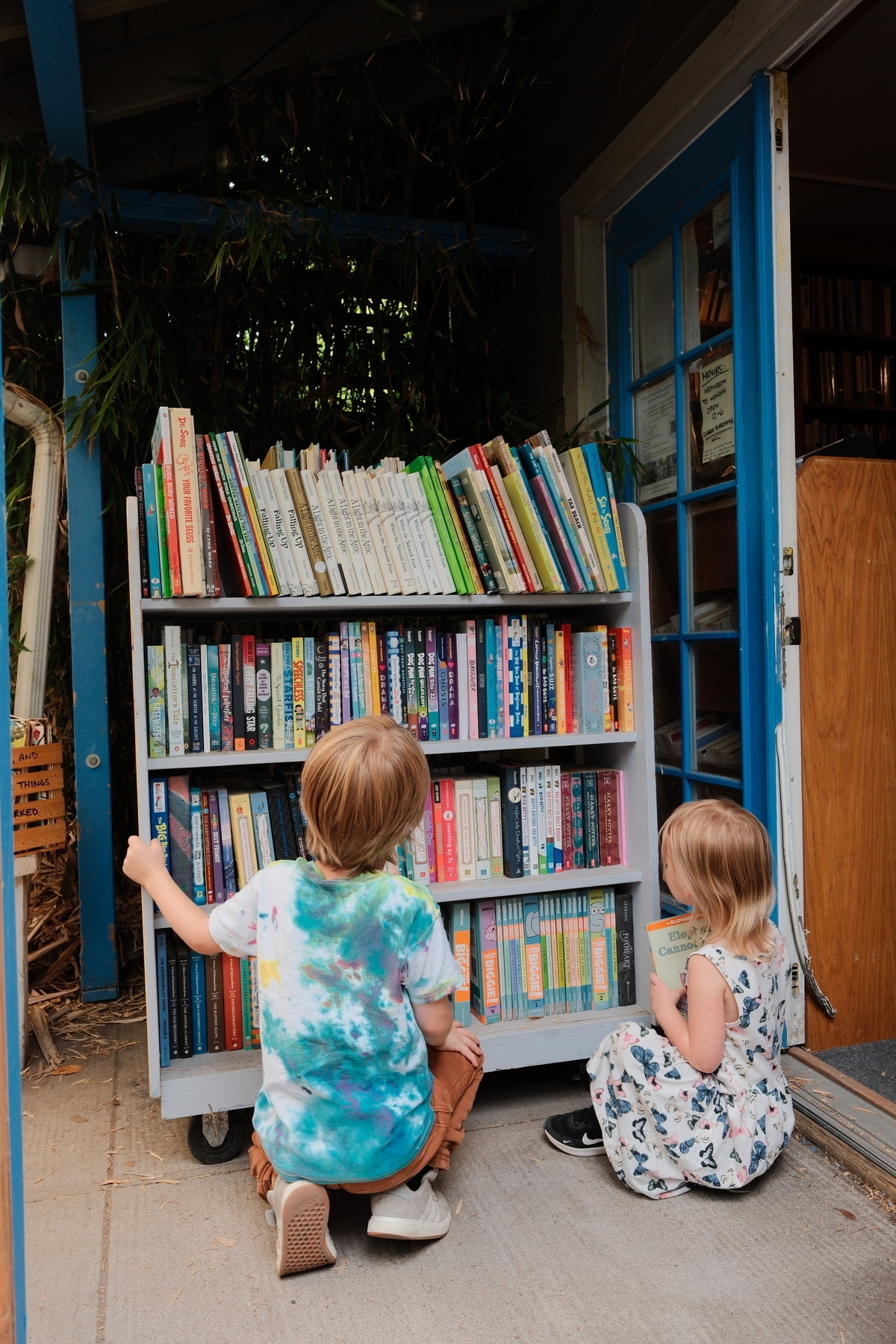 Two children are looking at a bookshelf filled with various colorful books.