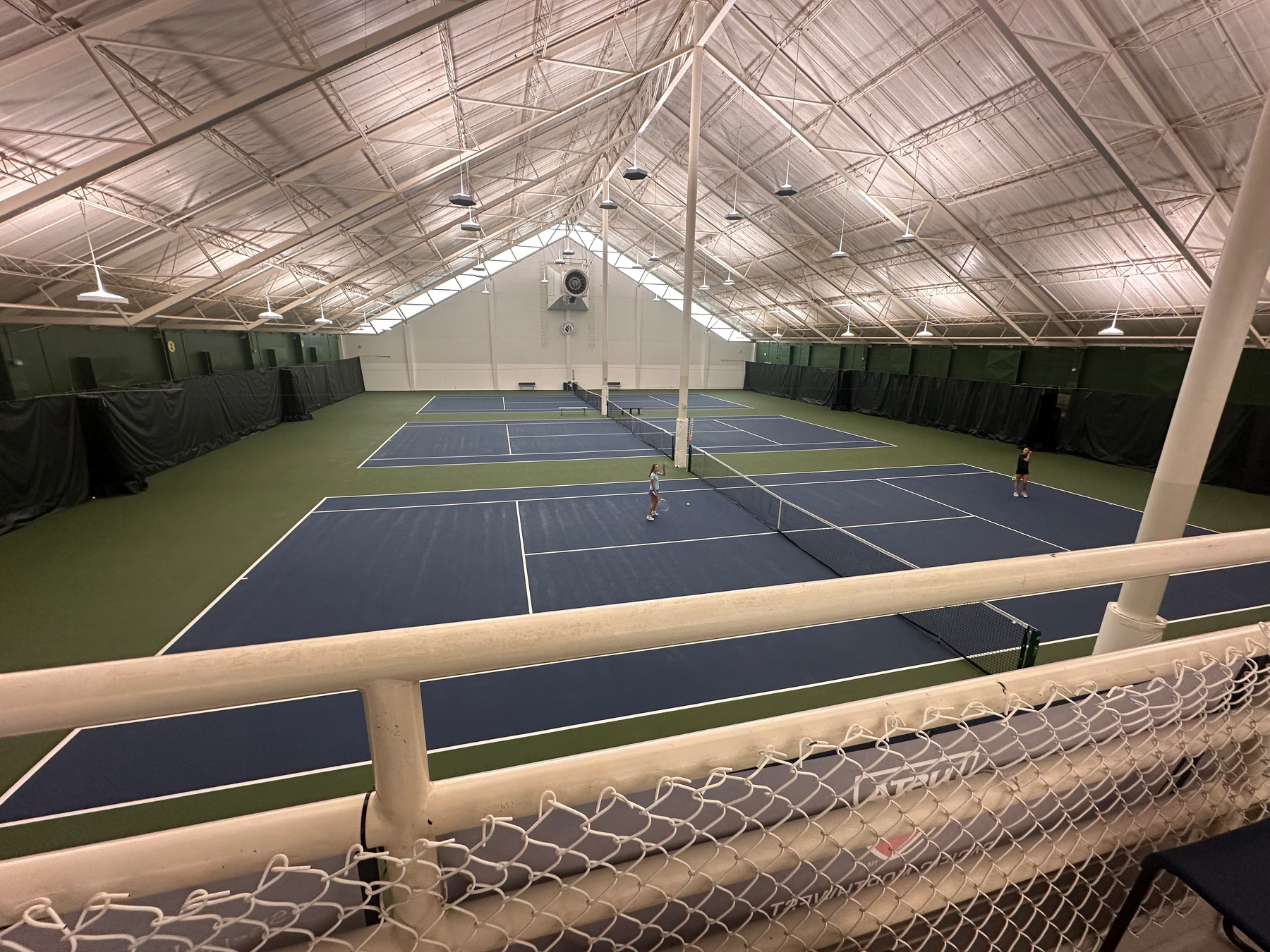 A spacious indoor tennis facility features multiple courts with a match in progress.